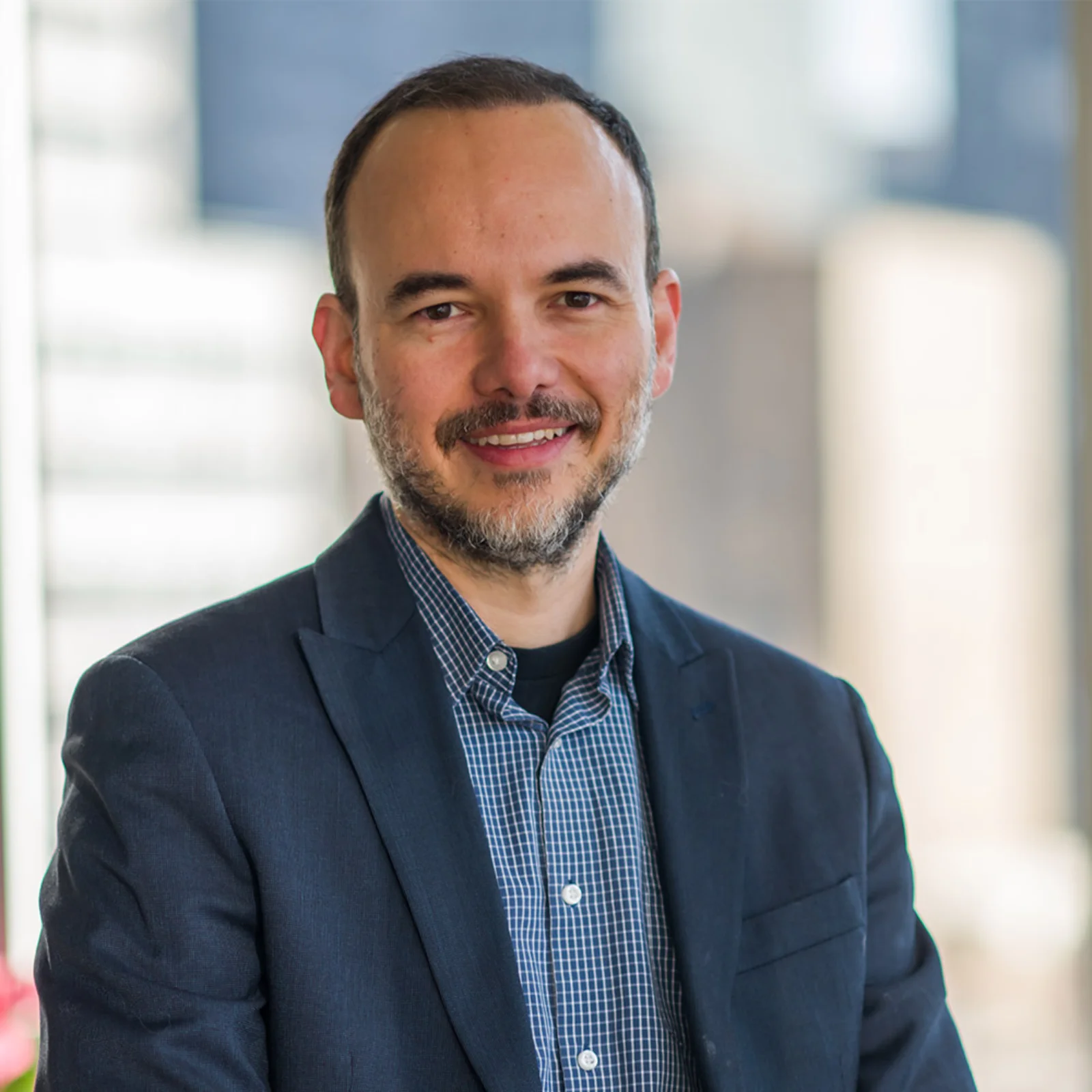 Portrait of Bruno Tinoco in a dark blazer and checked shirt.