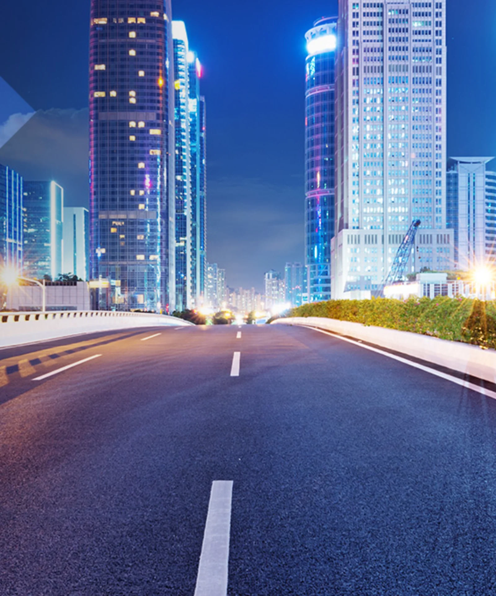 Empty urban road leading into a cityscape with brightly lit skyscrapers at night, symbolizing innovation and the future of urban development.