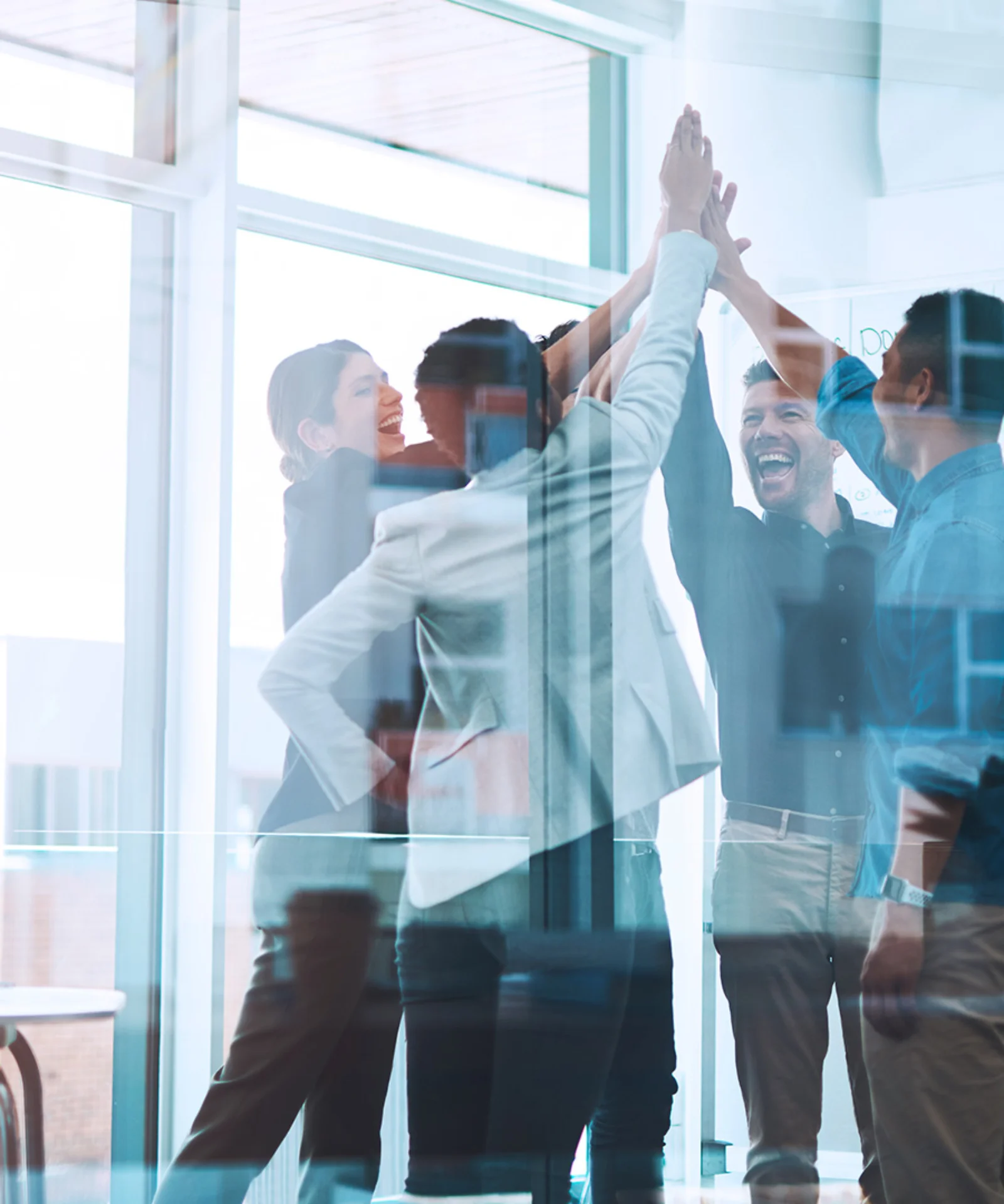 A group of professionals high-fiving in an office setting, celebrating a successful collaboration with whiteboards and brainstorming notes in the background.