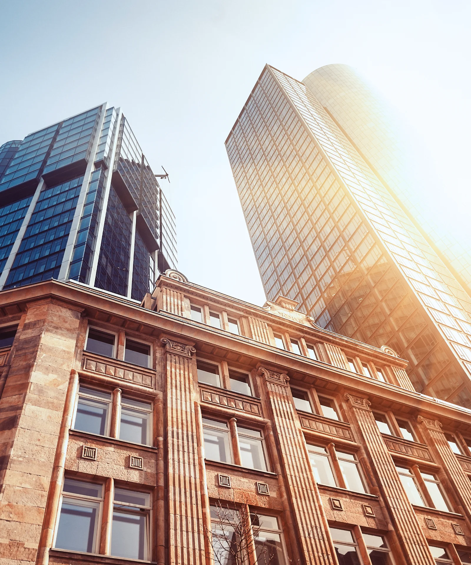 Hohes Gebäude aus der Froschperspektive mit strahlender Sonne und blauem Himmel im Hintergrund, dargestellt als Key Visual für Finanzdienstleistungen.