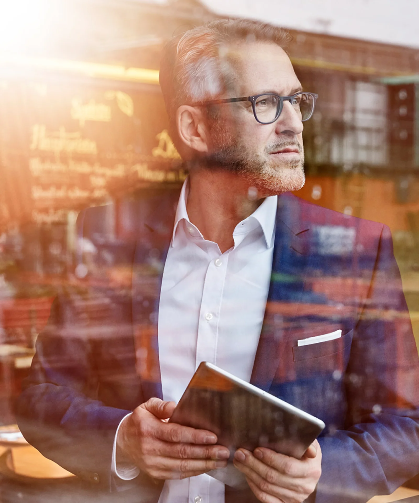 Business professional holding a tablet and looking through a cafe window, representing GFT&#039;s focus on digital transformation and strategic innovation.