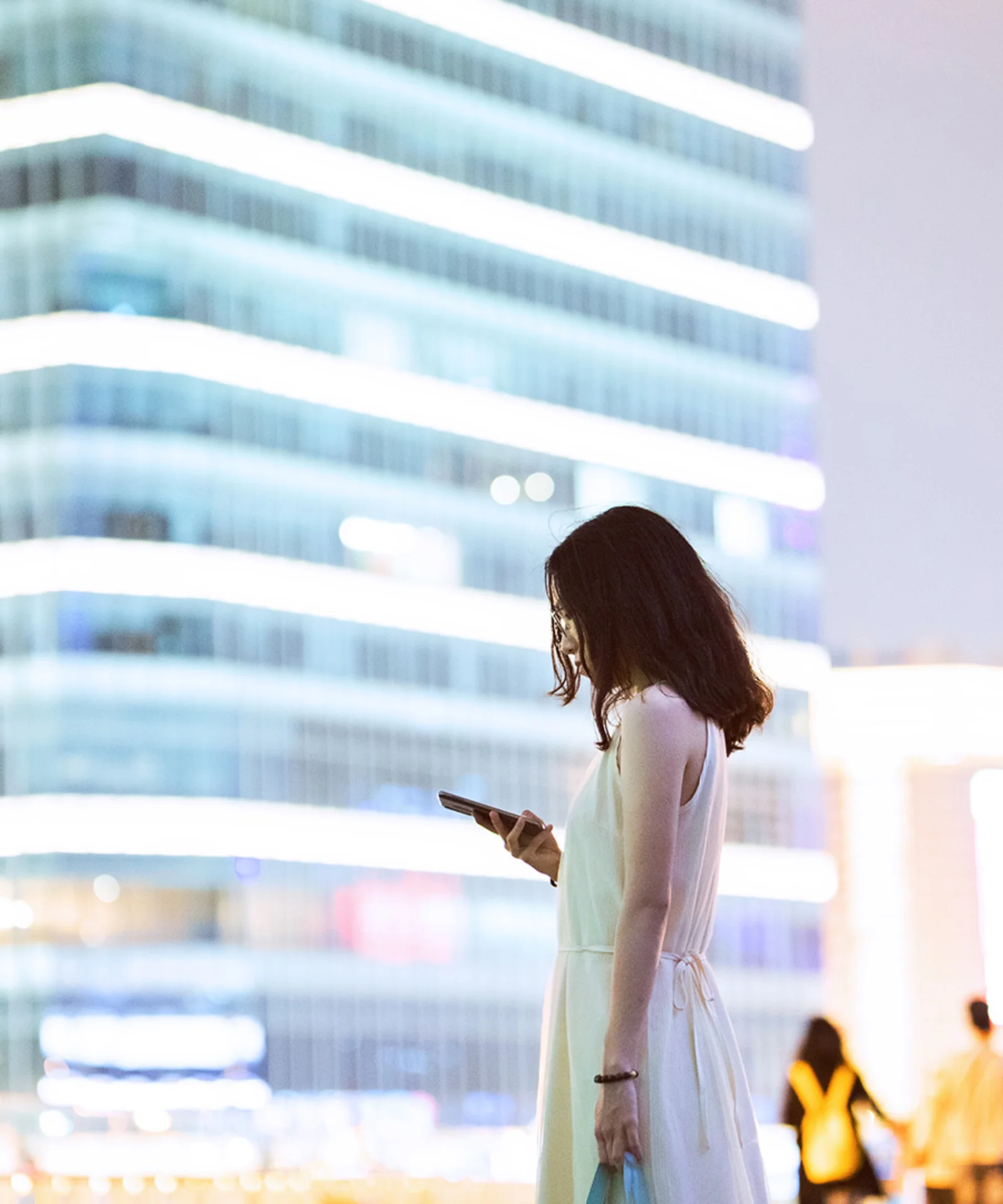 Uma mulher profissional usando seu smartphone com uma paisagem urbana moderna ao fundo, simbolizando o impacto das Moedas Digitais de Bancos Centrais (CBDCs) no futuro do setor bancário comercial.