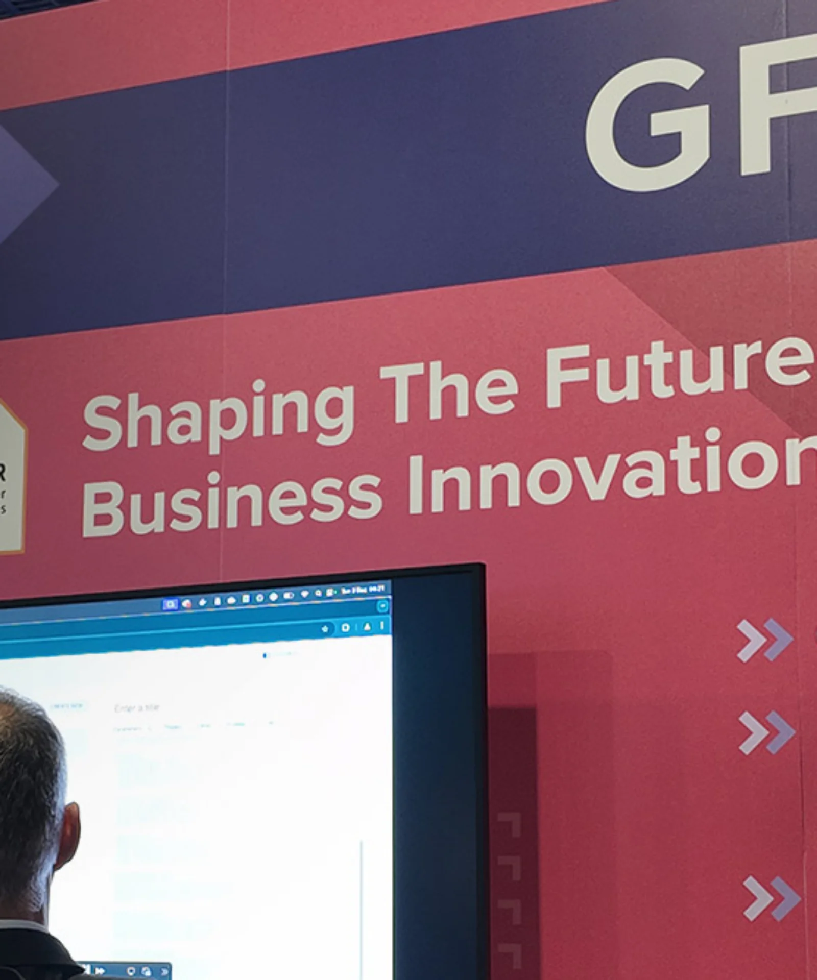 GFT exhibition booth with a banner reading &quot;Shaping the Future of Business Innovation,&quot; highlighting services such as Generative AI, Platform Modernization, and Visual Inspection. Two individuals are interacting with a screen showcasing GFT technology solutions.