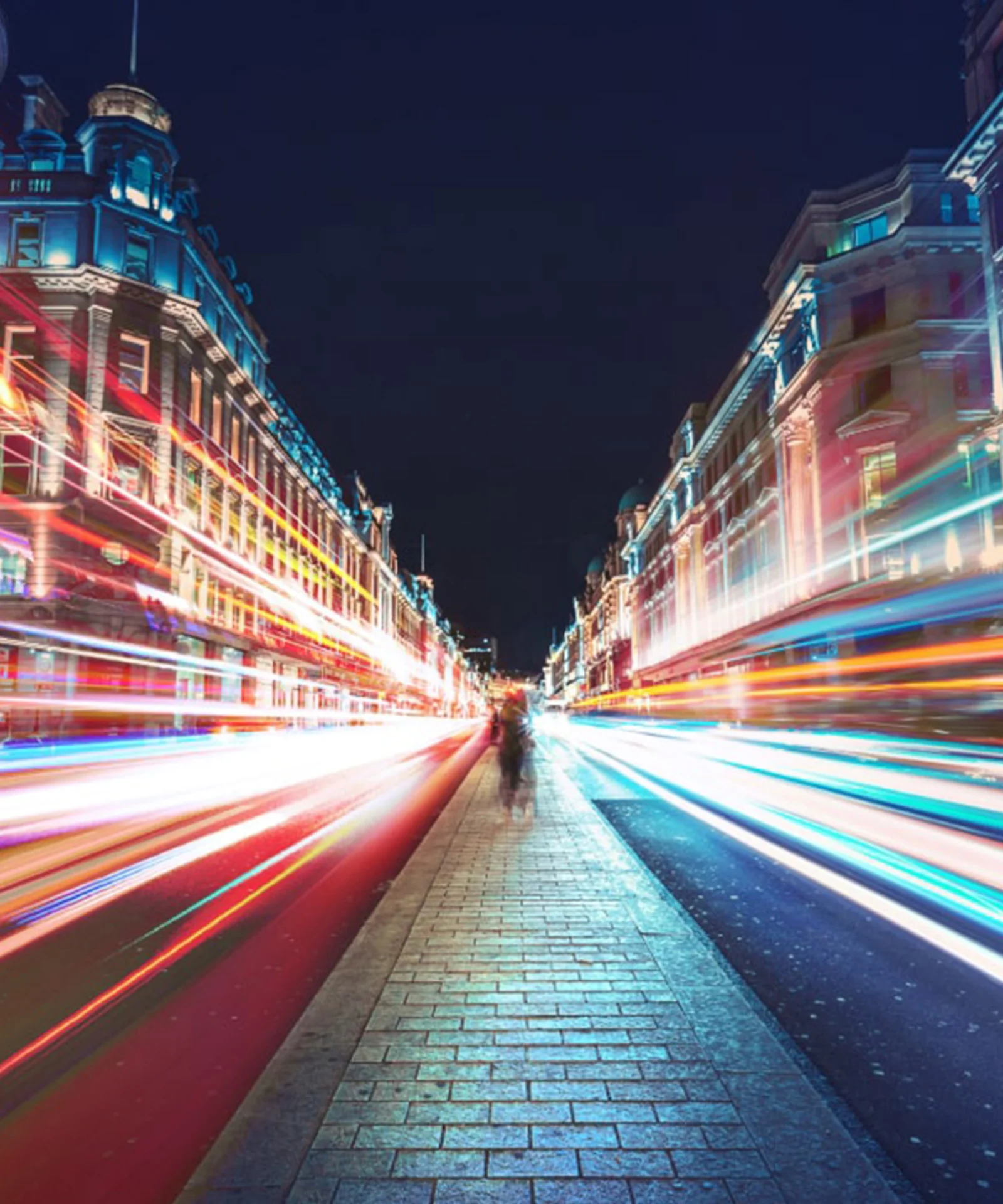 A vibrant city street at night, illuminated by streaks of colorful lights, representing the fast-paced and dynamic nature of modern banking and finance.