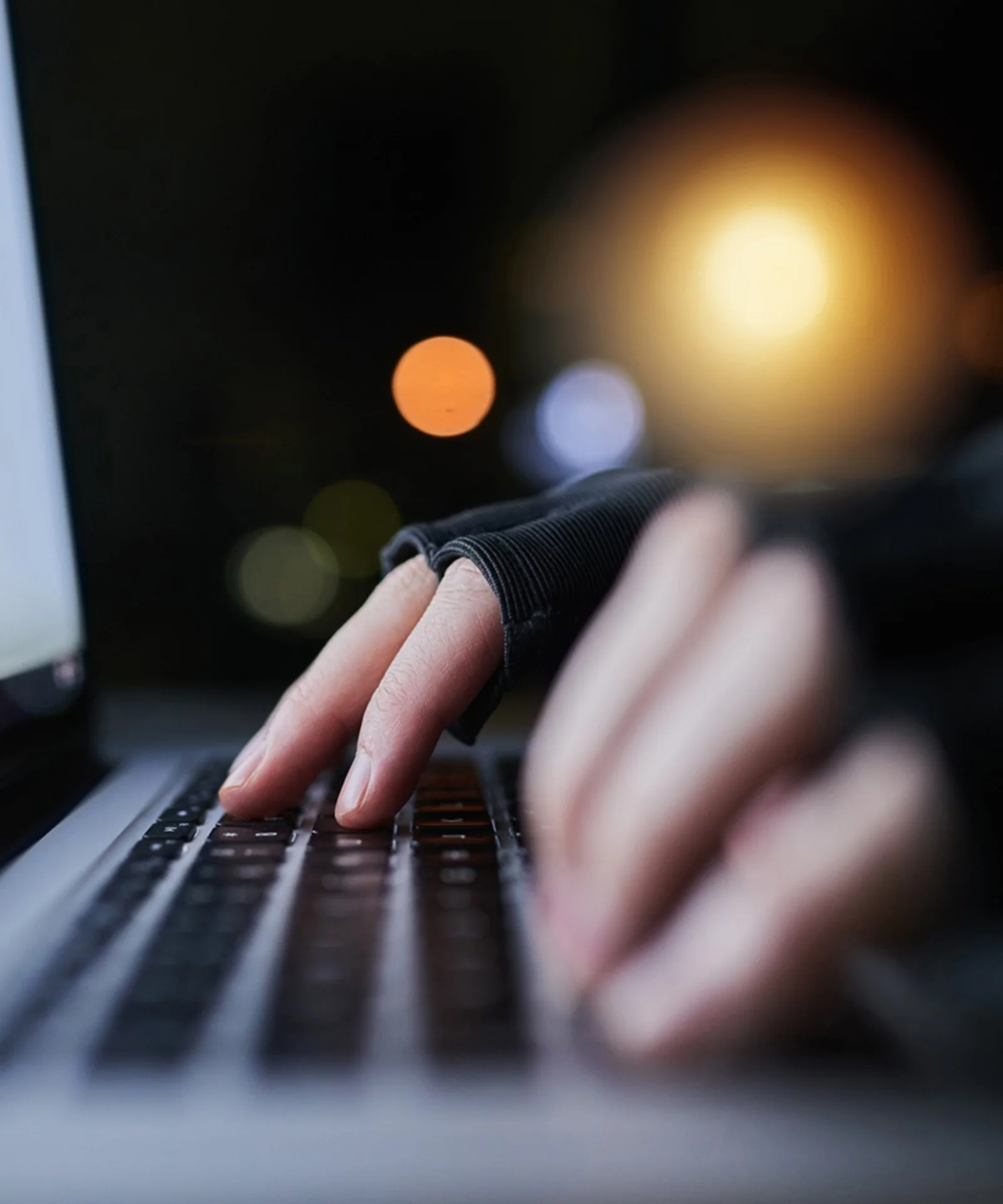 Close-up of hands typing on a laptop keyboard in a dimly lit environment, symbolising the use of AI and big data to combat fraud.