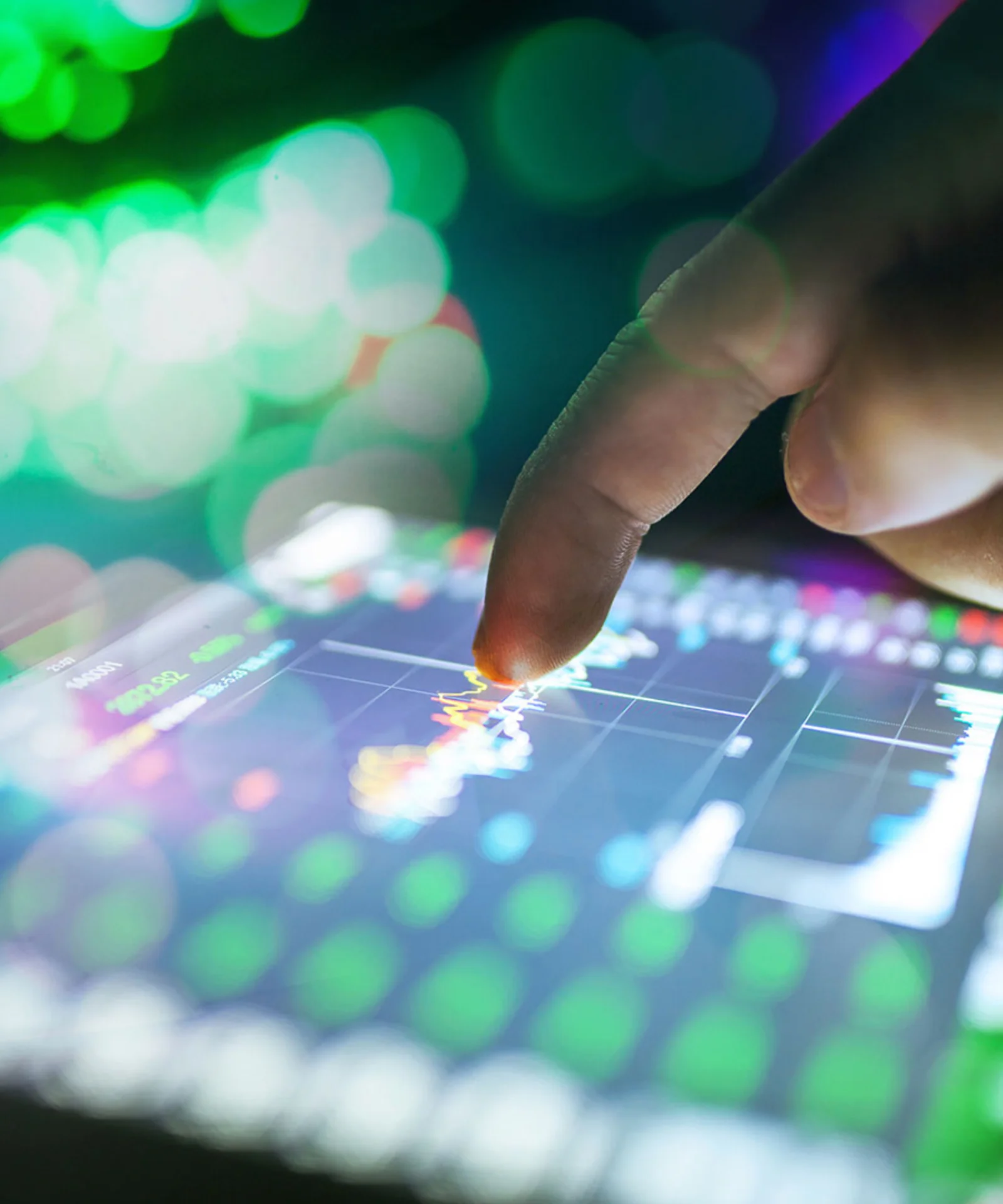 Close-up of a finger interacting with a touchscreen displaying energy management data, with vibrant green and colorful bokeh lights in the background.