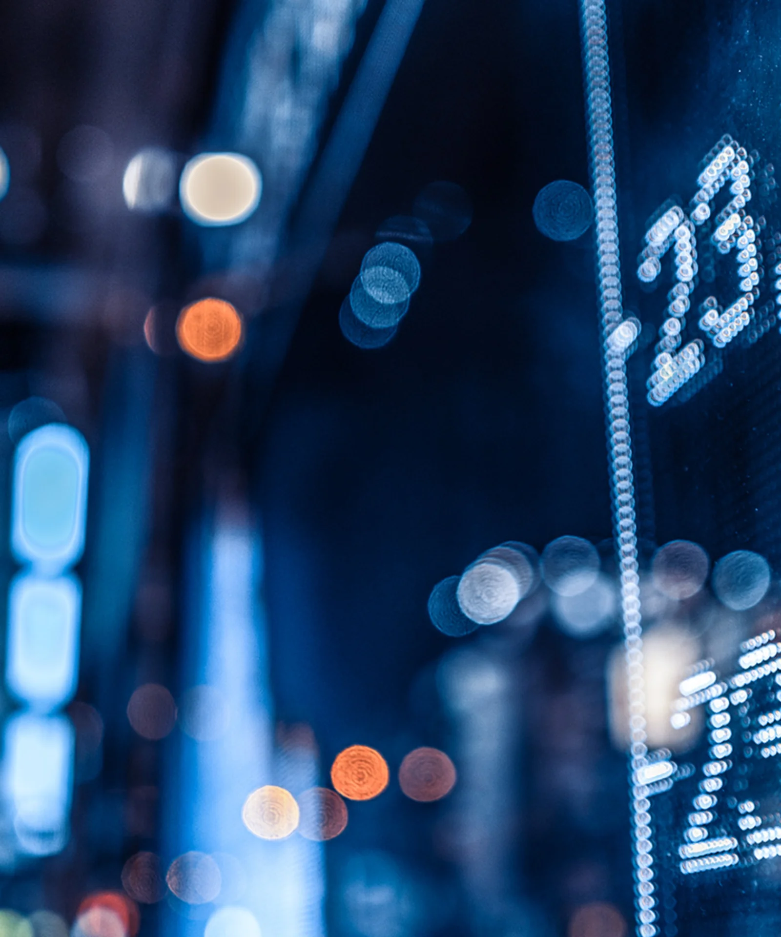 Close-up of a digital stock market display board with blurred city lights in the background, highlighting numbers and financial data.