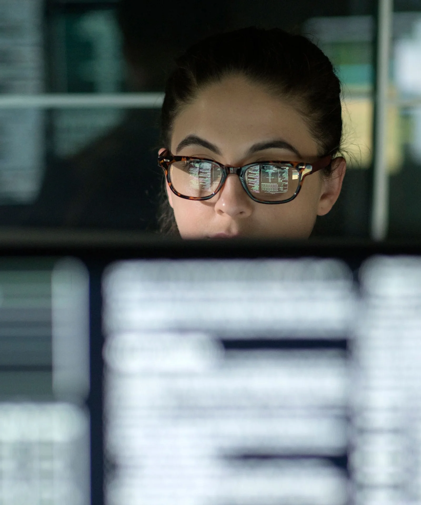 A woman wearing glasses concentrates on her work, with lines of code reflecting in her lenses, symbolising the dedication and precision in software development.