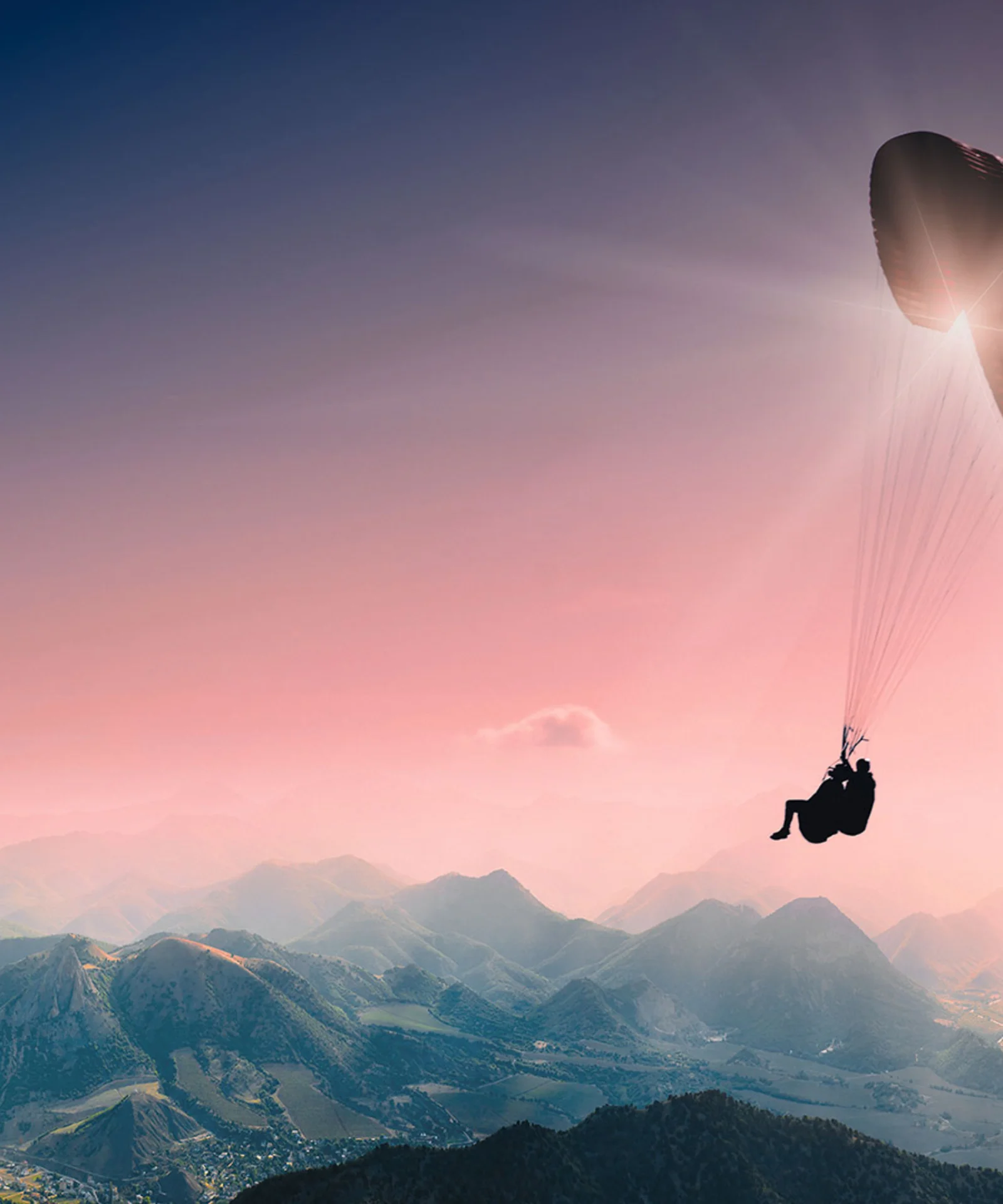 A paraglider floating above a vast landscape of mountains at sunset, symbolising the expansive opportunities and freedom provided by GFT’s cloud technology solutions.