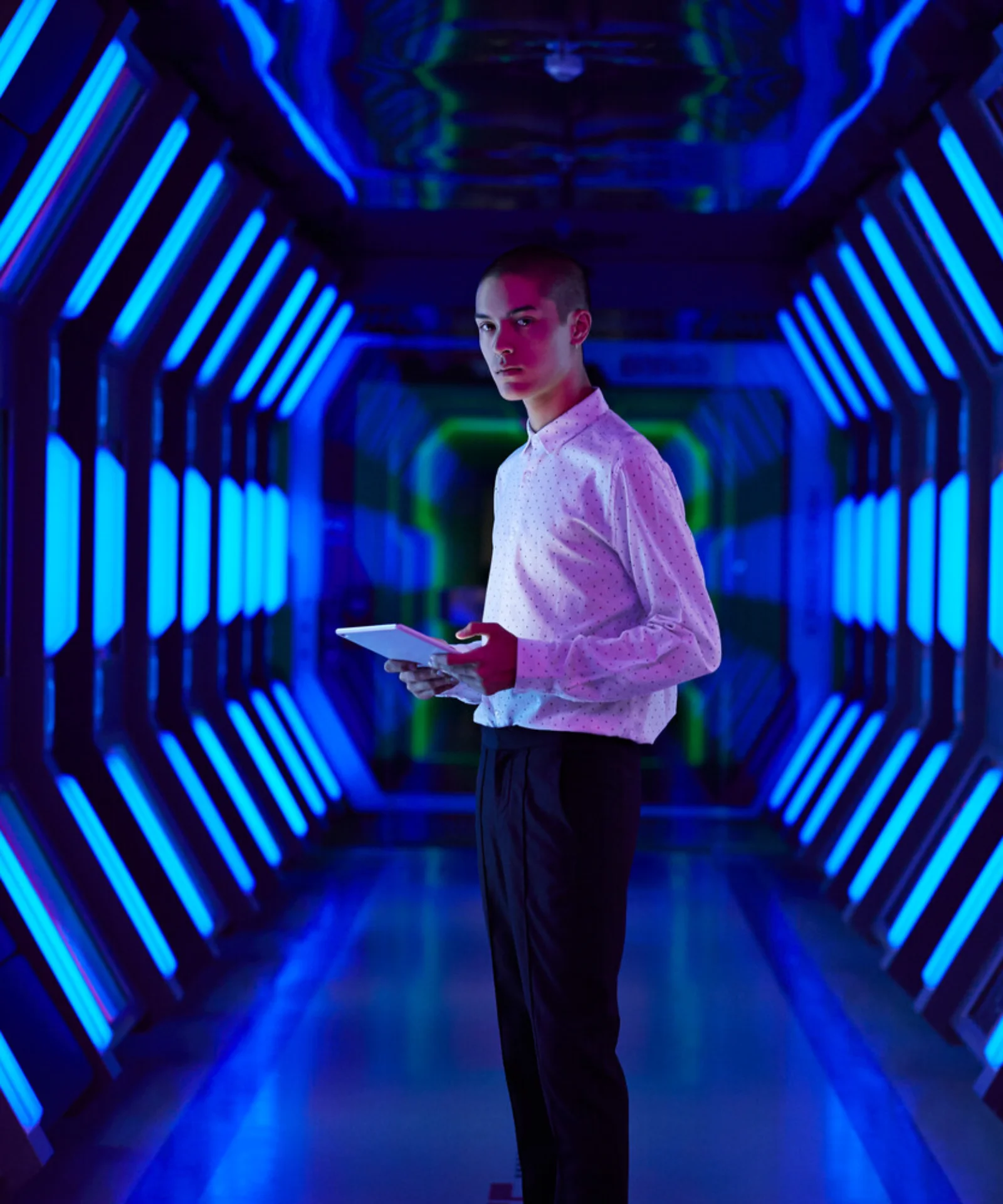 A person holding a tablet standing in a futuristic hallway with vibrant blue lighting, representing the advanced and innovative environment of AWS Kubernetes.