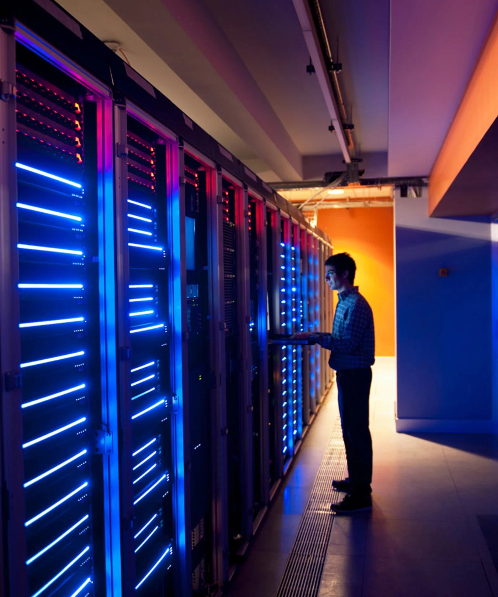 Technician working in a data centre with blue and red illuminated servers