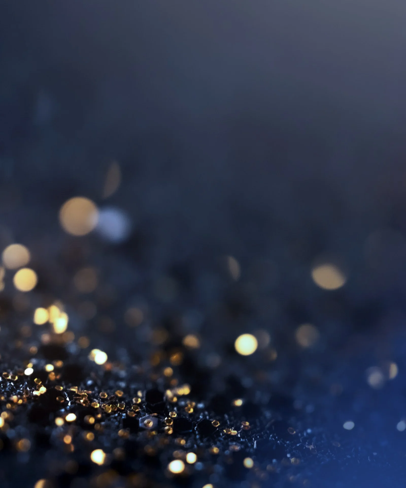 Abstract close-up of golden and blue sparkling lights on a dark surface, with soft bokeh effects in the background.