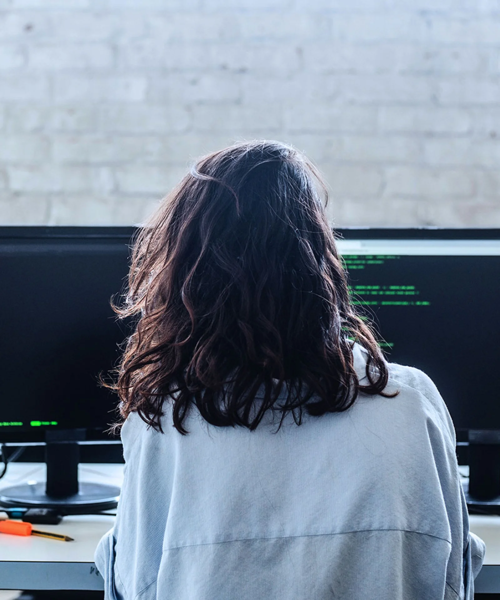 A young professional working at a dual-monitor setup in an industrial-style office, representing the growth of tech talents