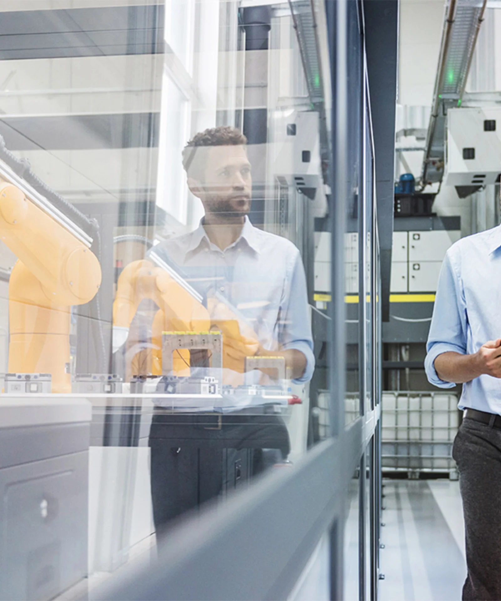 A professional engineer holding a tablet walks through a modern factory with advanced robotic arms working behind glass partitions.