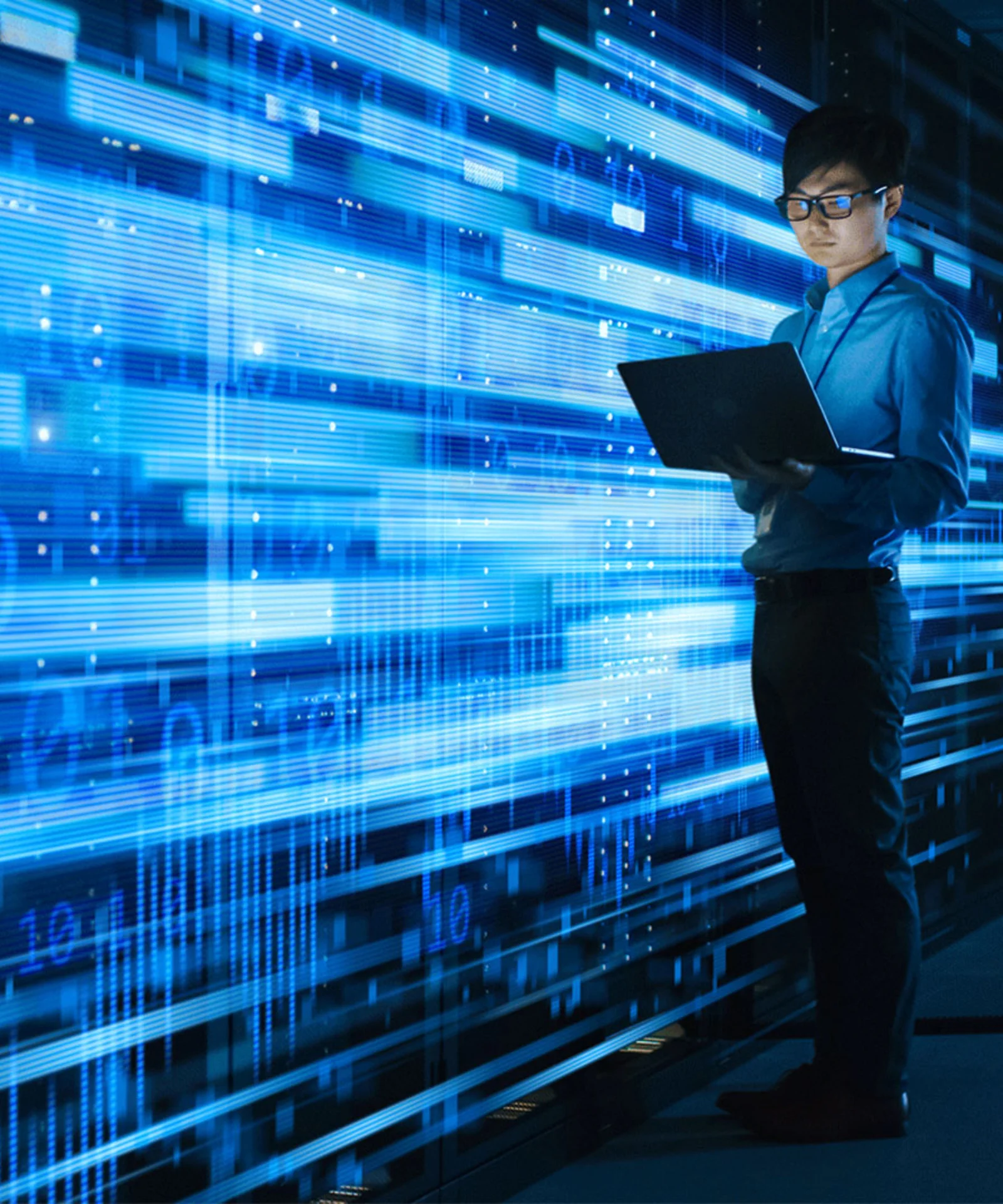 A person in a blue shirt working on a laptop, standing in a server room filled with racks of servers and digital displays. Bright blue data streams and graphics overlay the scene, representing data processing and cloud computing.