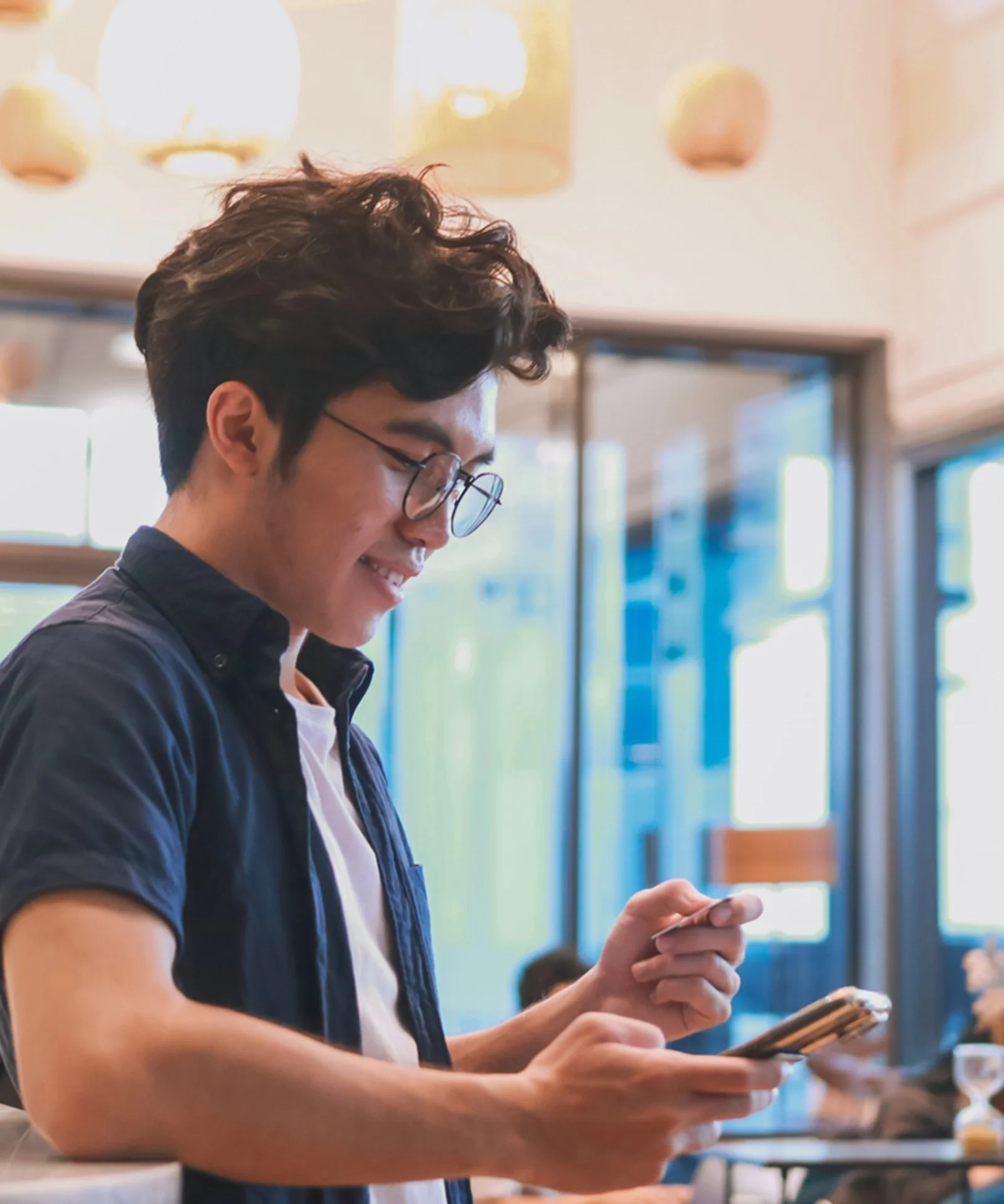 A young man using his smartphone and holding a credit card in a modern café, representing the use of a mobile push notifications platform by a retail bank.