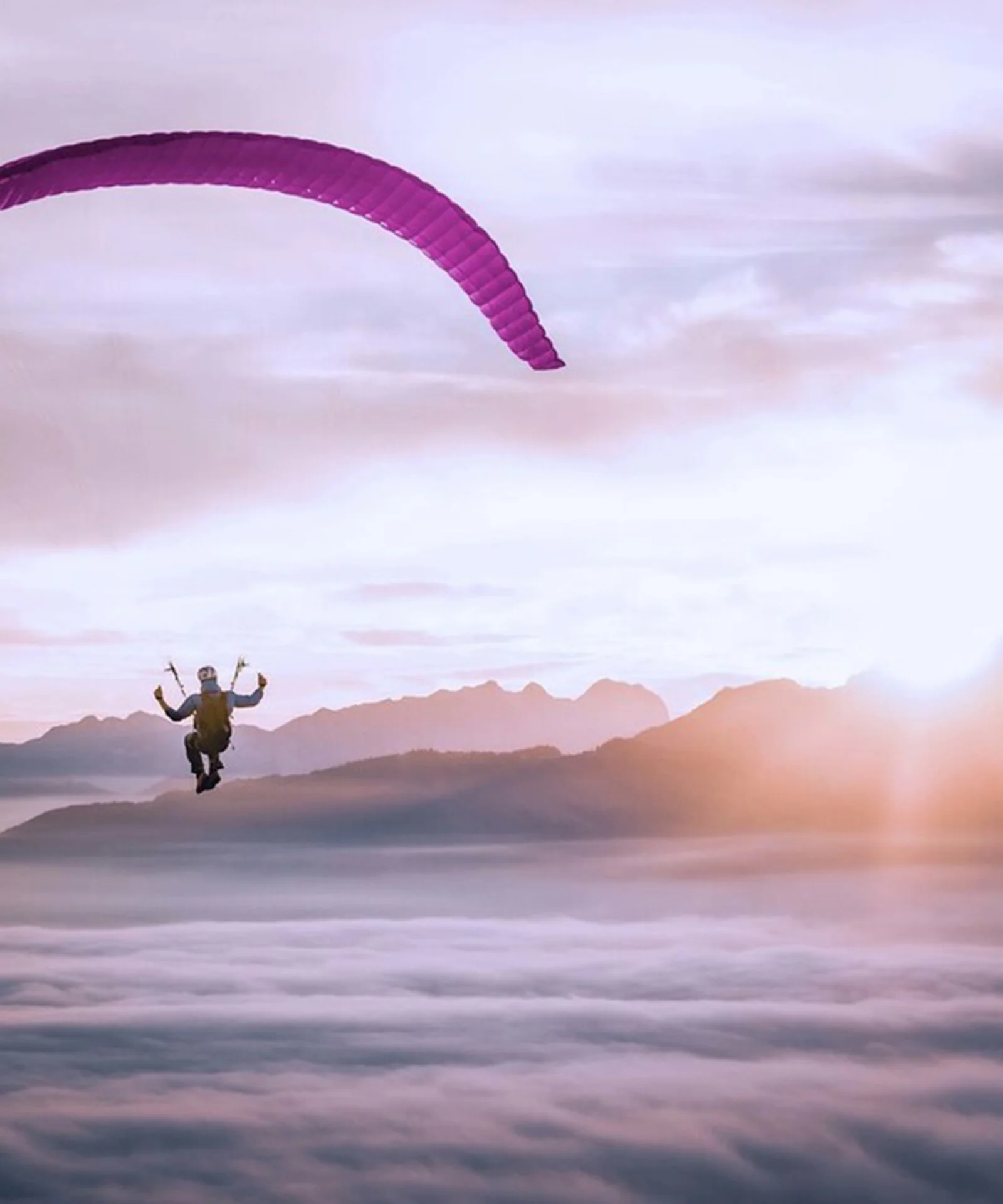 Cette image à couper le souffle capture l&#039;essence de la liberté et de l&#039;aventure alors qu&#039;un parapentiste solitaire s&#039;élève gracieusement au-dessus d&#039;une couverture de nuages. Le parapente, avec sa voile violette vibrante, se dresse sur le magnifique fond d&#039;un lever de soleil, projetant une lueur chaude et dorée sur la scène. Les sommets lointains des montagnes s&#039;élèvent au-dessus de la couche nuageuse, ajoutant de la profondeur et un sens de l&#039;échelle à l&#039;image. L&#039;atmosphère sereine et impressionnante met en valeur la beauté du parapente et la perspective unique qu&#039;il offre sur le monde. Ce visuel résume parfaitement le frisson et la tranquillité du vol en plein air.