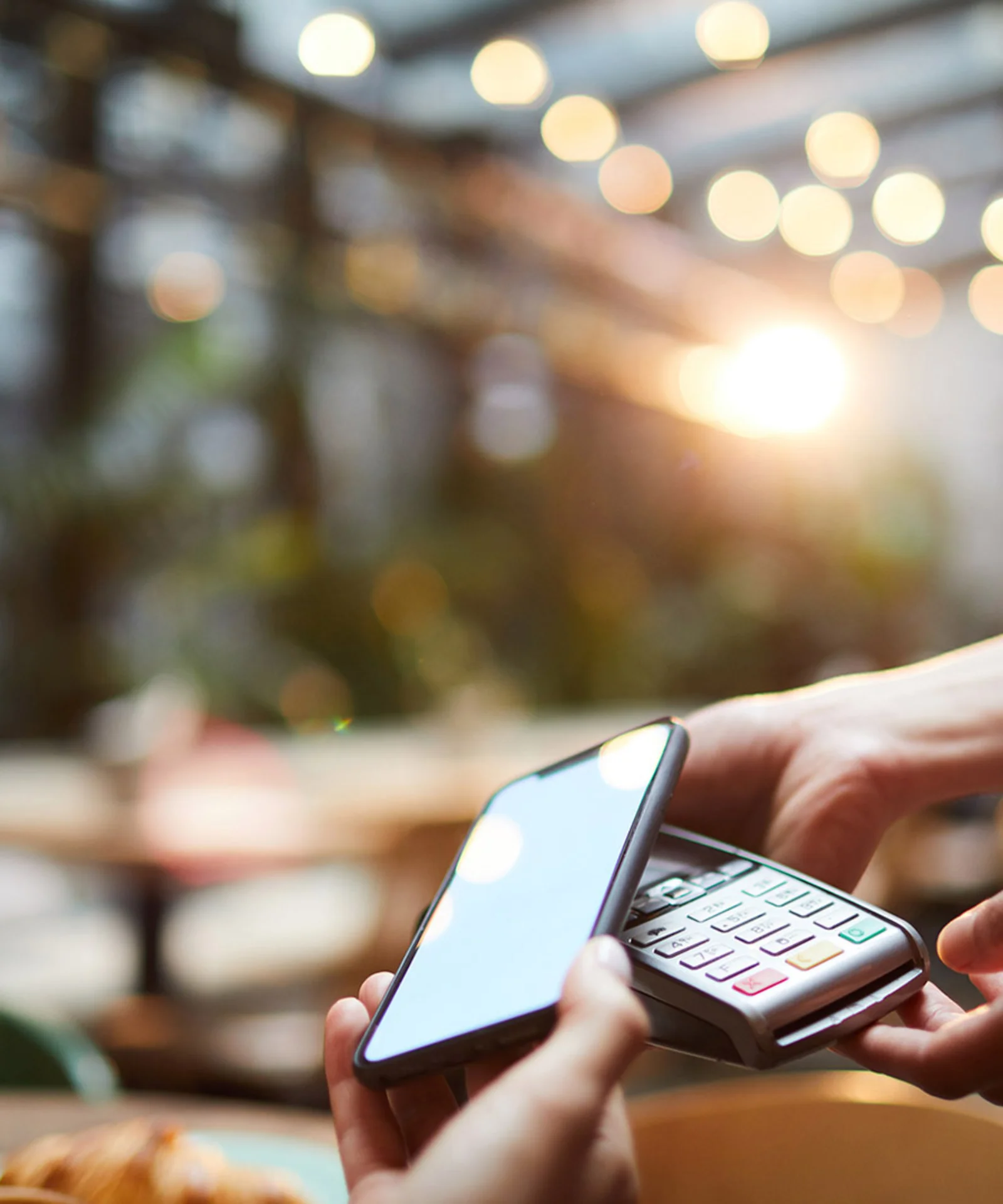 Close-up of a person making a mobile payment with a smartphone in a modern cafe, highlighting GFT&#039;s digital payment solutions