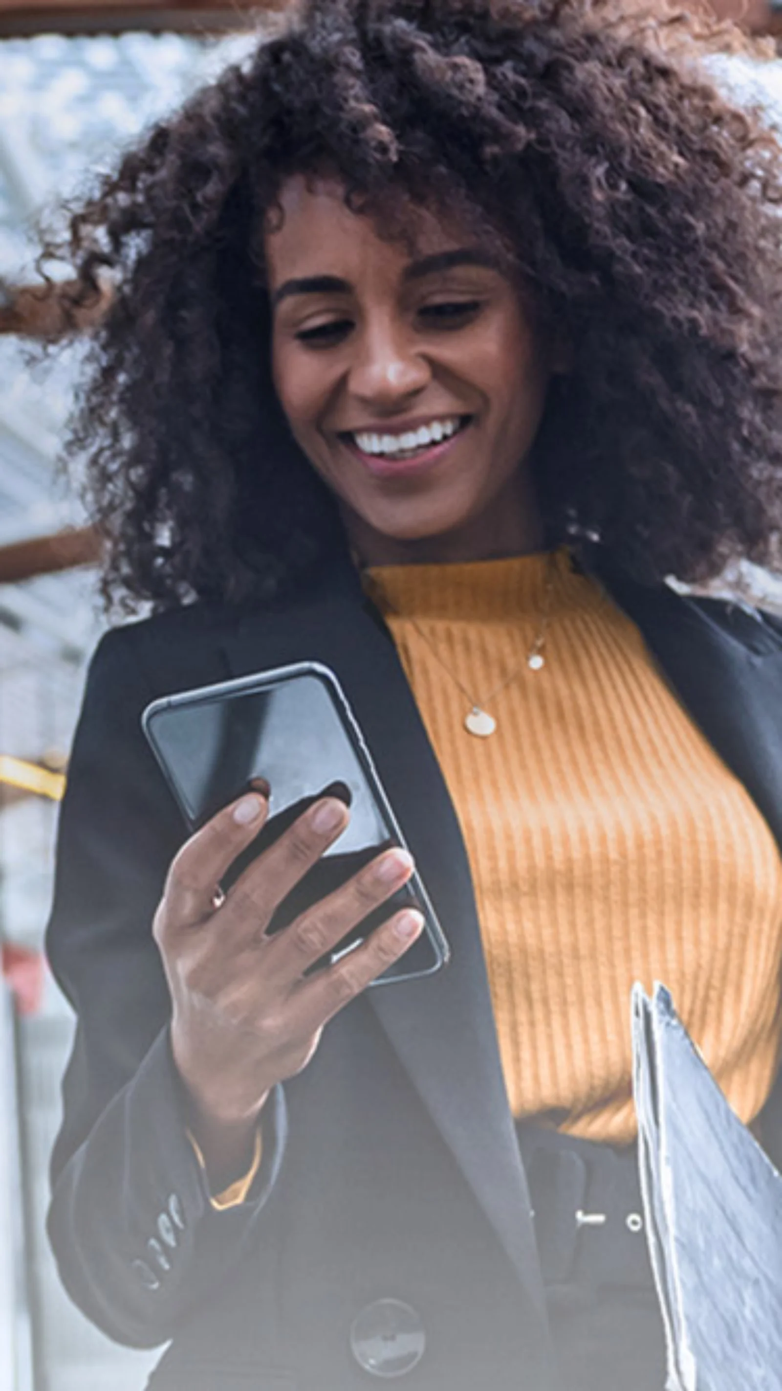 Smiling businesswoman using a smartphone while riding an escalator in a modern building with glass and metal architecture.