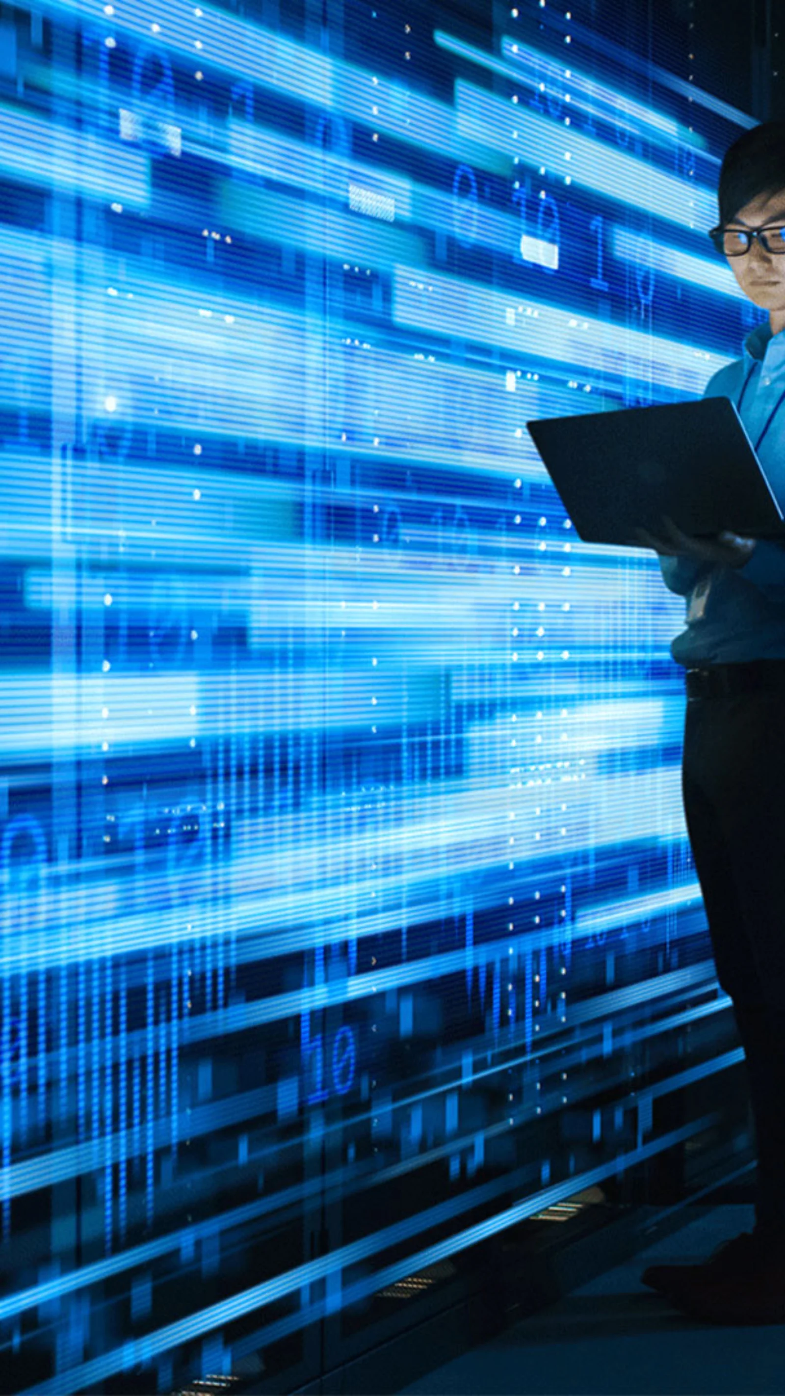 A person in a blue shirt working on a laptop, standing in a server room filled with racks of servers and digital displays. Bright blue data streams and graphics overlay the scene, representing data processing and cloud computing.