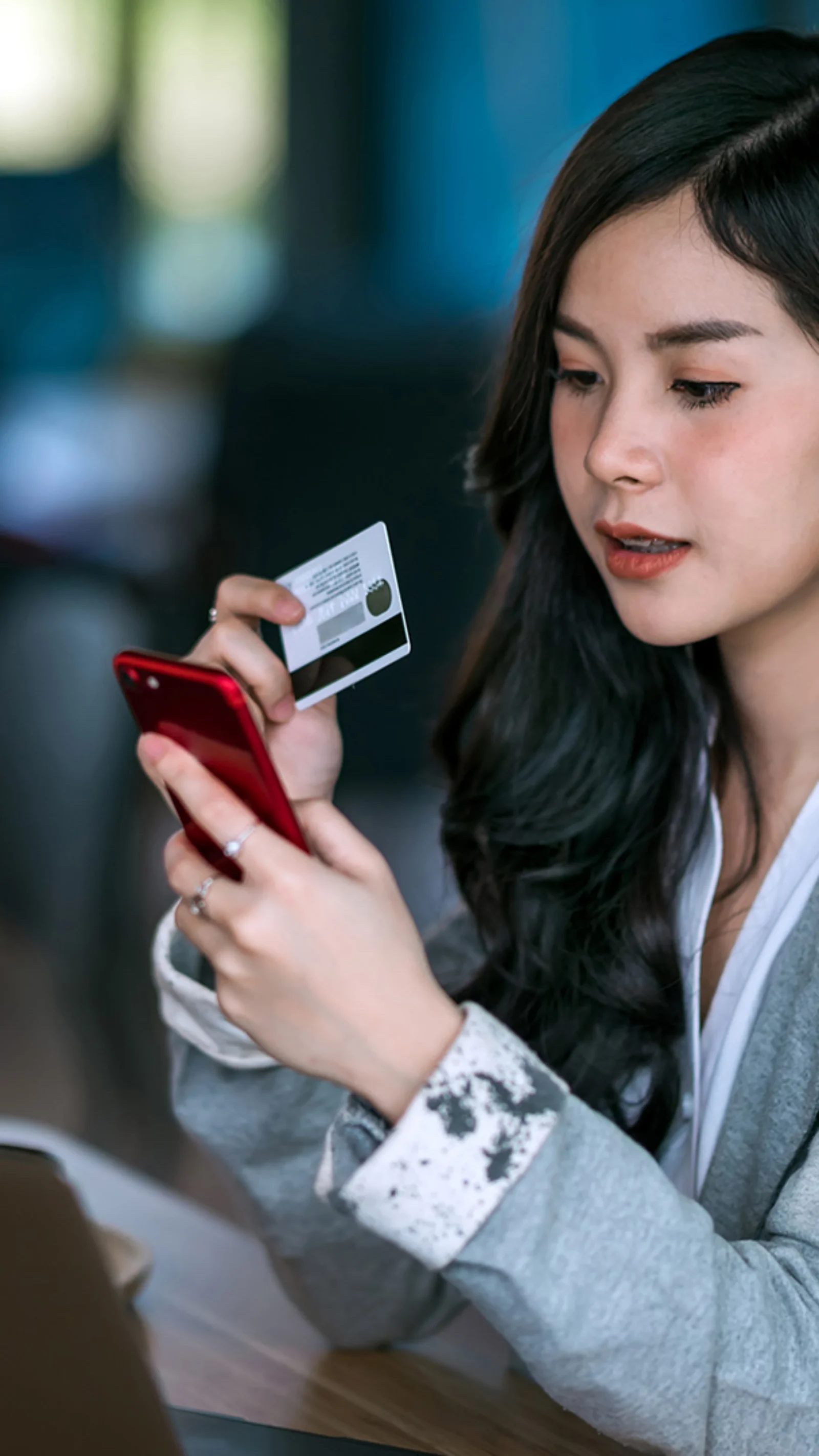 A woman using her smartphone and holding a credit card, showcasing the digital onboarding process through a mobile application.