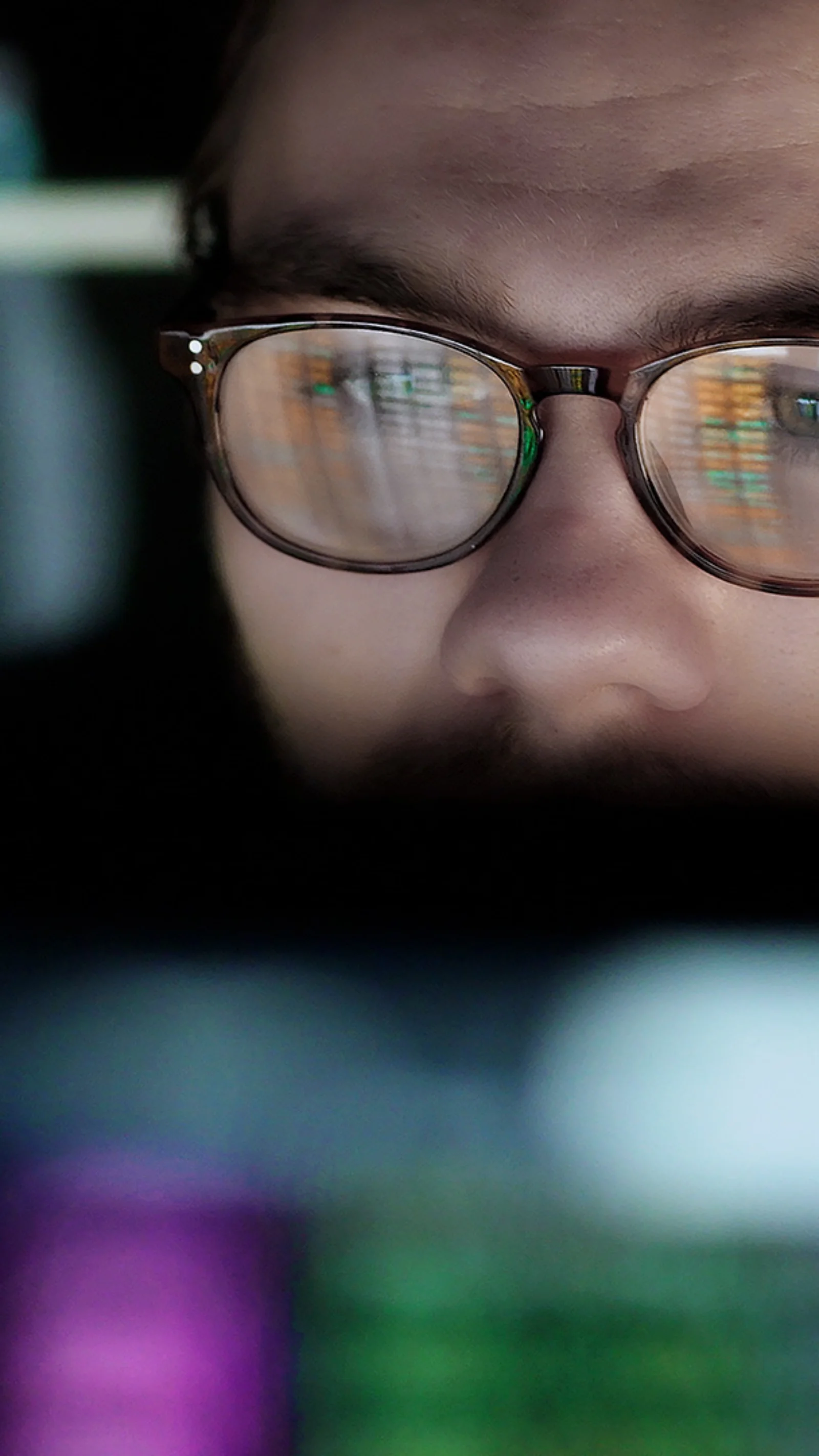 Close-up of a man wearing glasses, reflecting computer screens filled with data, representing the focus on machine learning operations (MLOps) in data-driven environments.