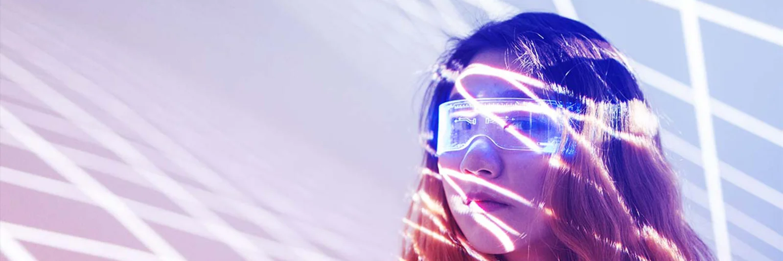 Esta imagen captura la esencia de la innovación con una estética futurista. Una mujer, ataviada con gafas de alta tecnología, está bañada por líneas de luz que se entrecruzan y crean un efecto visual dinámico y moderno. El fondo presenta tonos suaves de violeta y rosa, que realzan la sensación de avance tecnológico y visión de futuro. Esta imagen encarna a la perfección el espíritu de innovación de vanguardia y la integración de la tecnología en la vida cotidiana.