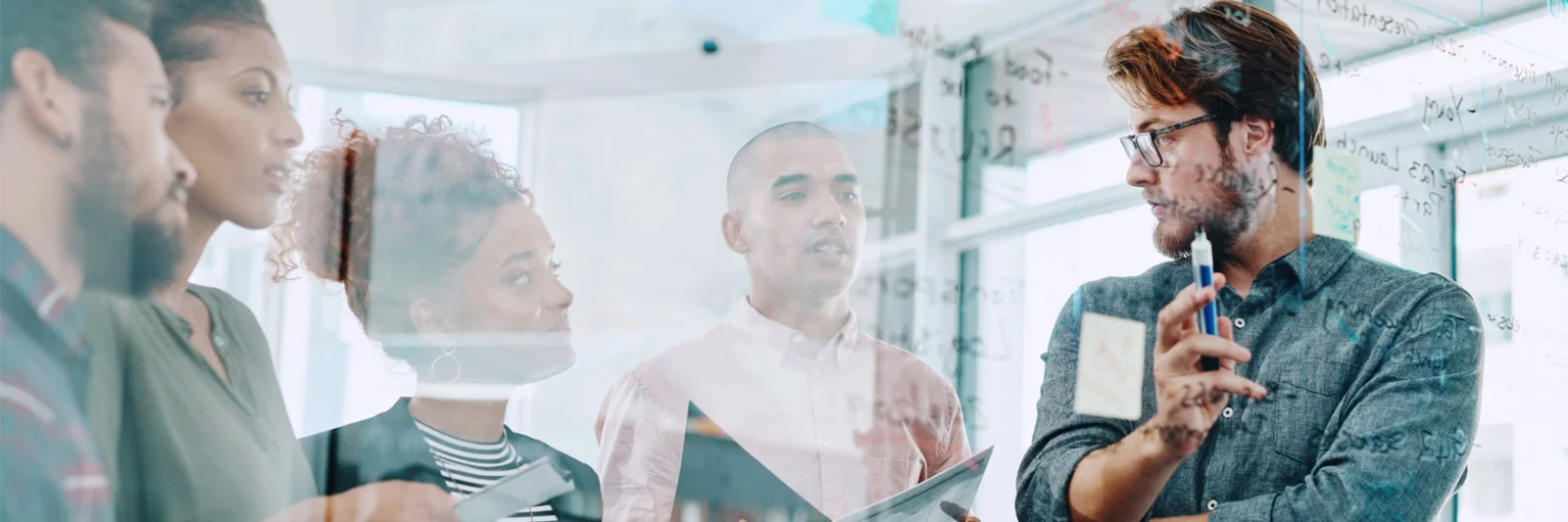 A group of diverse professionals collaborating and brainstorming ideas on a glass board in a modern office setting