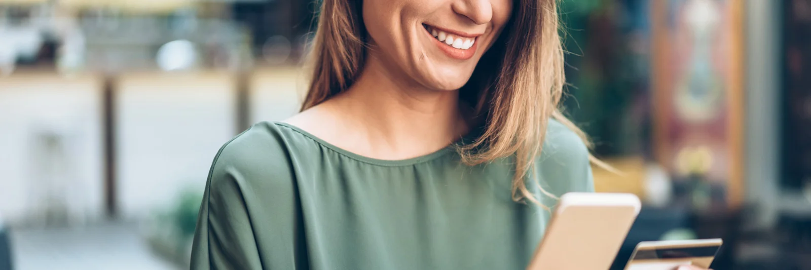 Uma mulher sorridente usando um smartphone e segurando um cartão de crédito, representando a conveniência de um novo aplicativo móvel de banco empresarial.