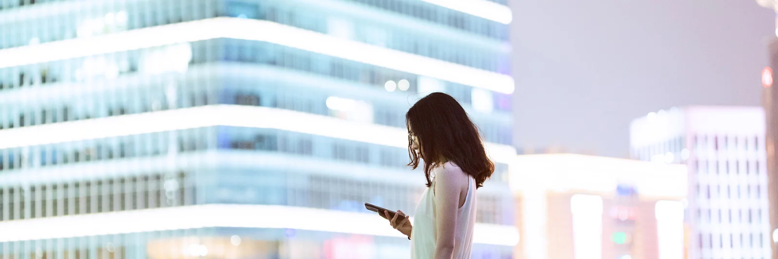 A professional woman using her smartphone with a modern cityscape in the background, symbolizing the impact of Central Bank Digital Currencies (CBDCs) on the future of commercial banking.