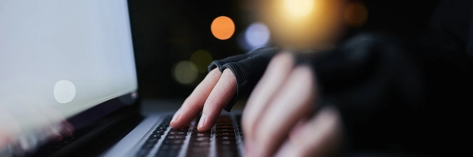 Close-up of hands typing on a laptop keyboard in a dimly lit environment, symbolising the use of AI and big data to combat fraud.