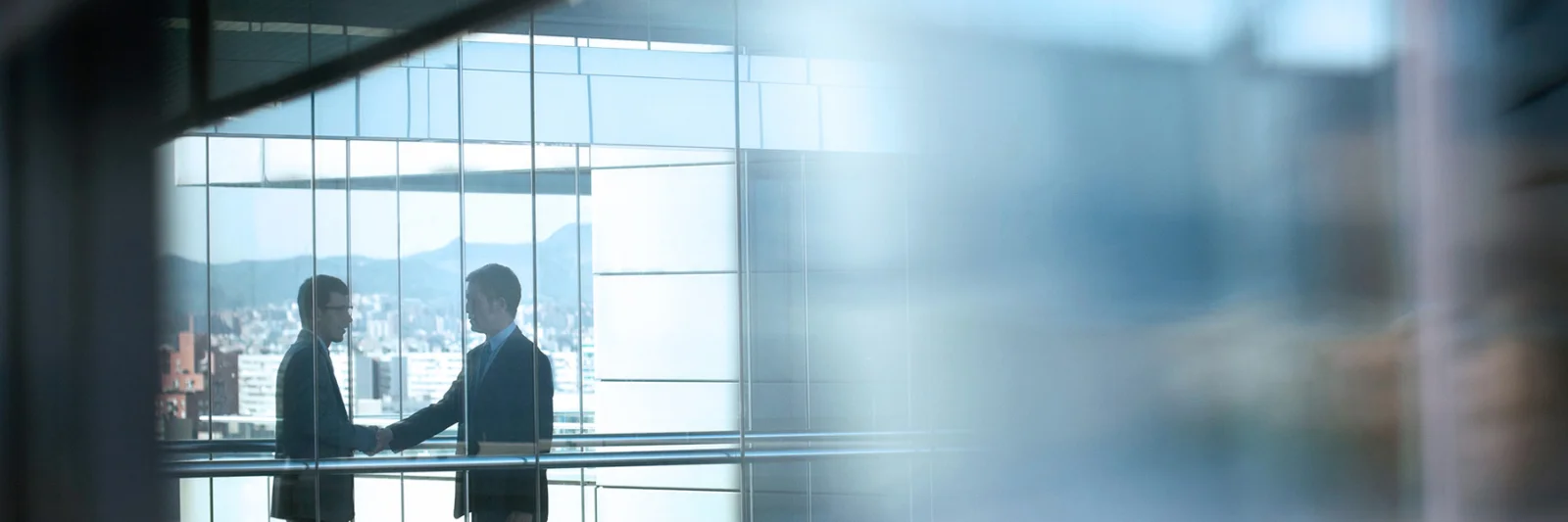 Two business professionals shaking hands in a modern office building with a cityscape in the background