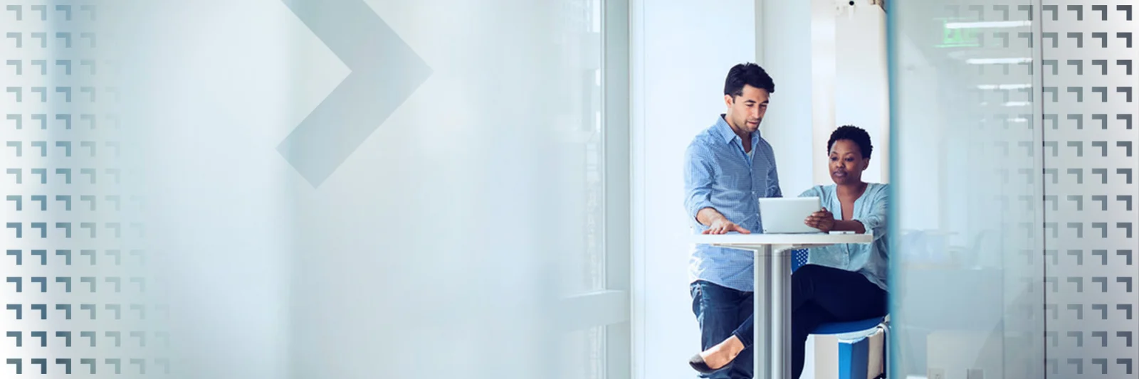 Two colleagues collaborating on a project while working on a laptop in a bright, modern office setting.