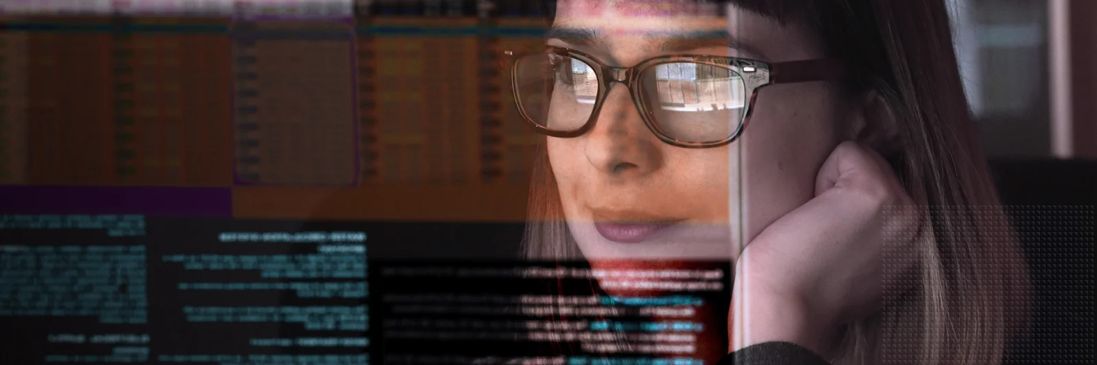 A woman wearing glasses intently looks at multiple programming screens with lines of code and data reflected in her glasses, representing software development and data analysis.