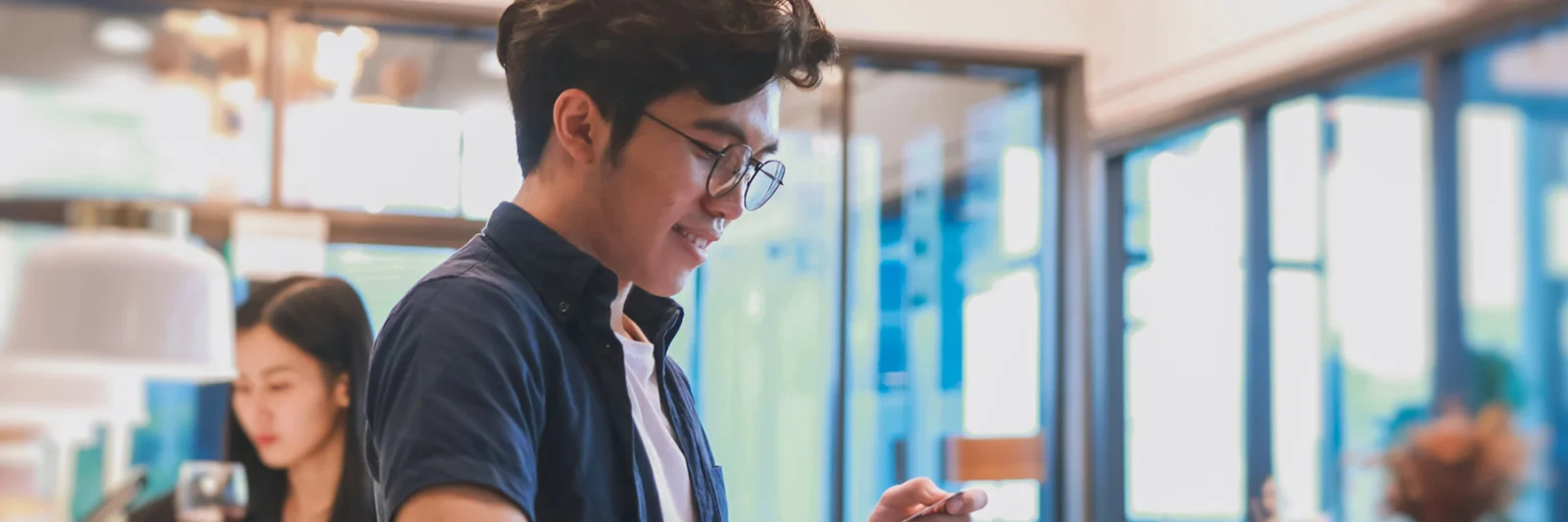 A young man using his smartphone and holding a credit card in a modern café, representing the use of a mobile push notifications platform by a retail bank.