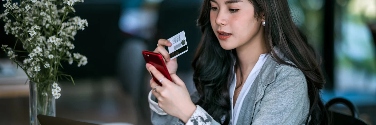 A woman using her smartphone and holding a credit card, showcasing the digital onboarding process through a mobile application.