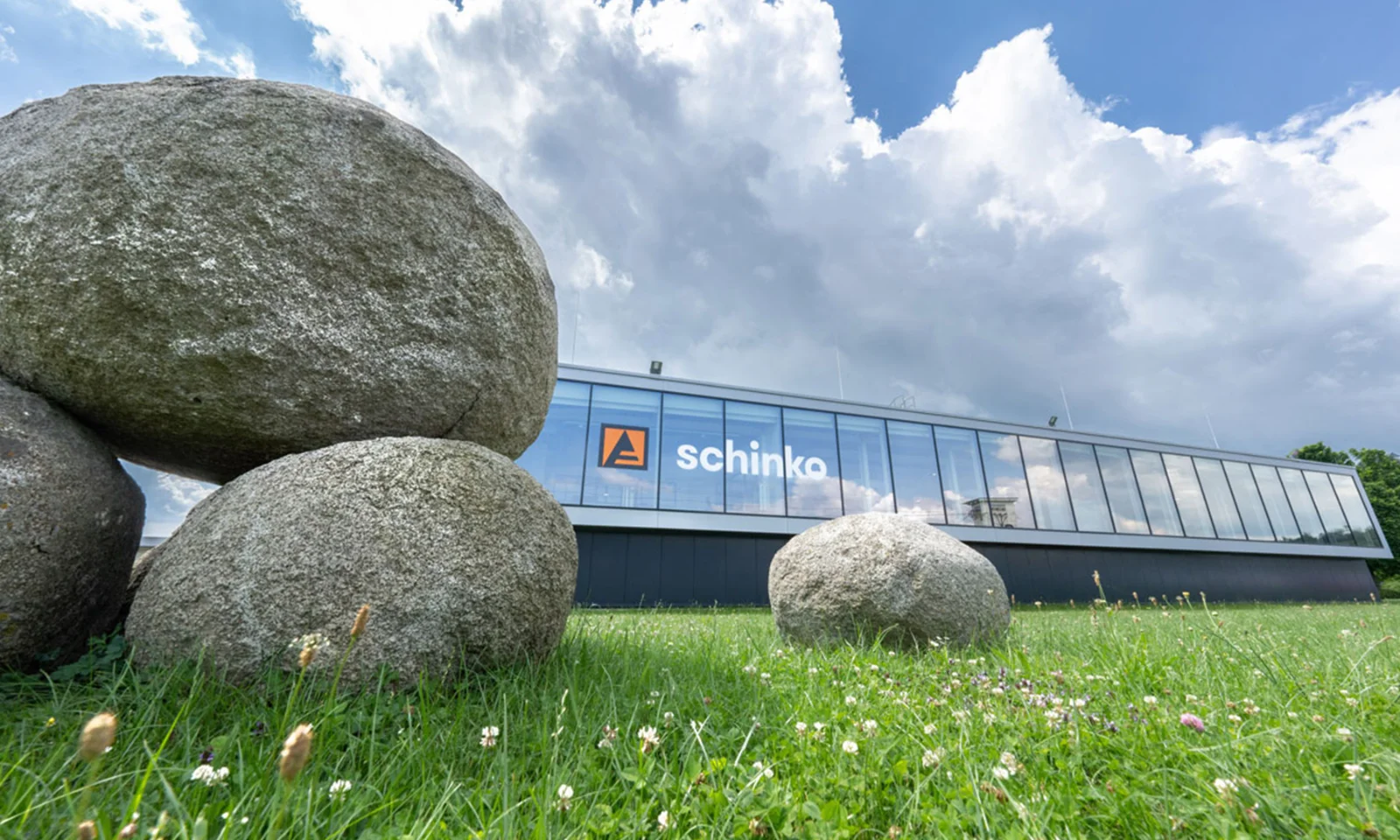 Exterior view of the Schinko facility, showcasing its modern architecture against a bright sky with large stone boulders in the foreground.