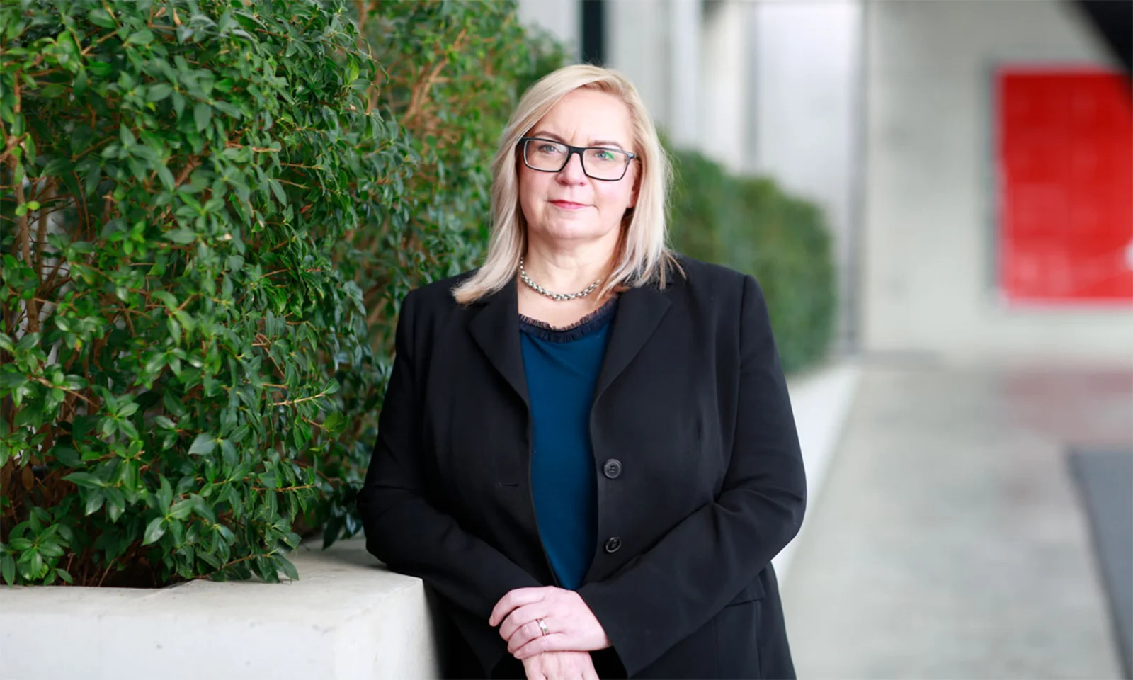 Marika Lulay, a member of the GFT Administrative Board, standing outdoors near green foliage, wearing a black blazer and glasses, symbolising focused leadership in the technology sector.