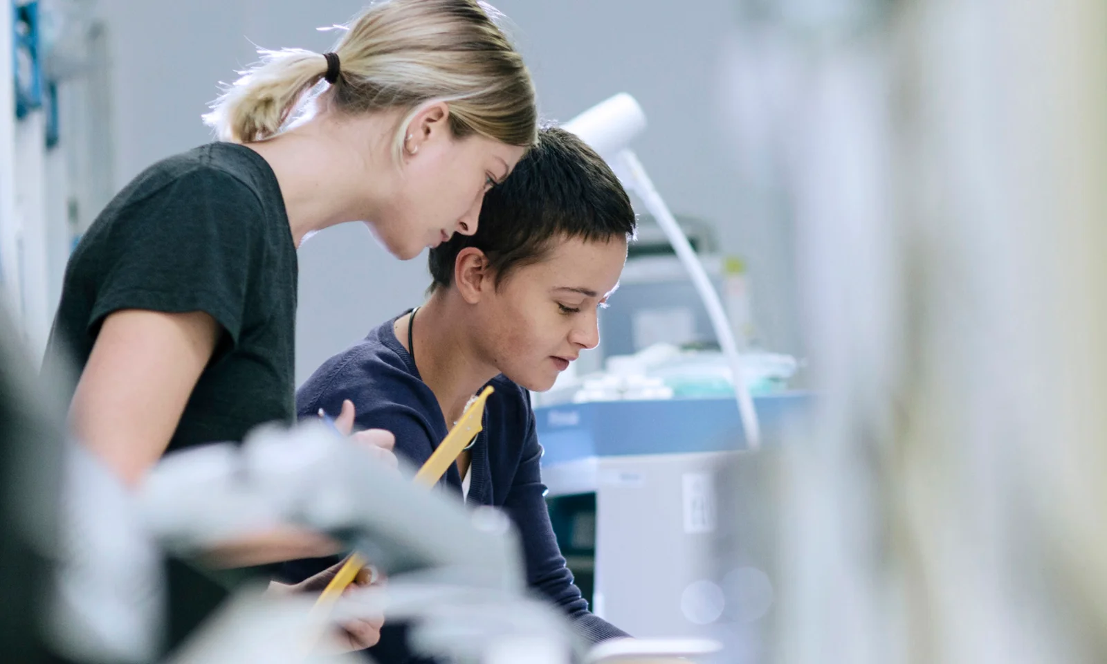 Two women deeply focused on their work in a modern tech lab, representing the contributions and involvement of women in the technology sector.