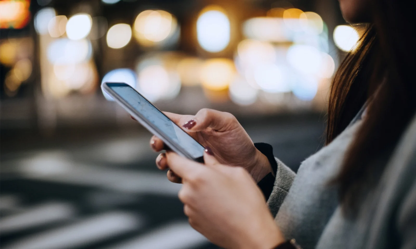 Close-up of a person using a smartphone at night, with a blurred cityscape in the background, illustrating the seamless and user-friendly mobile banking experience provided by Bankstart.