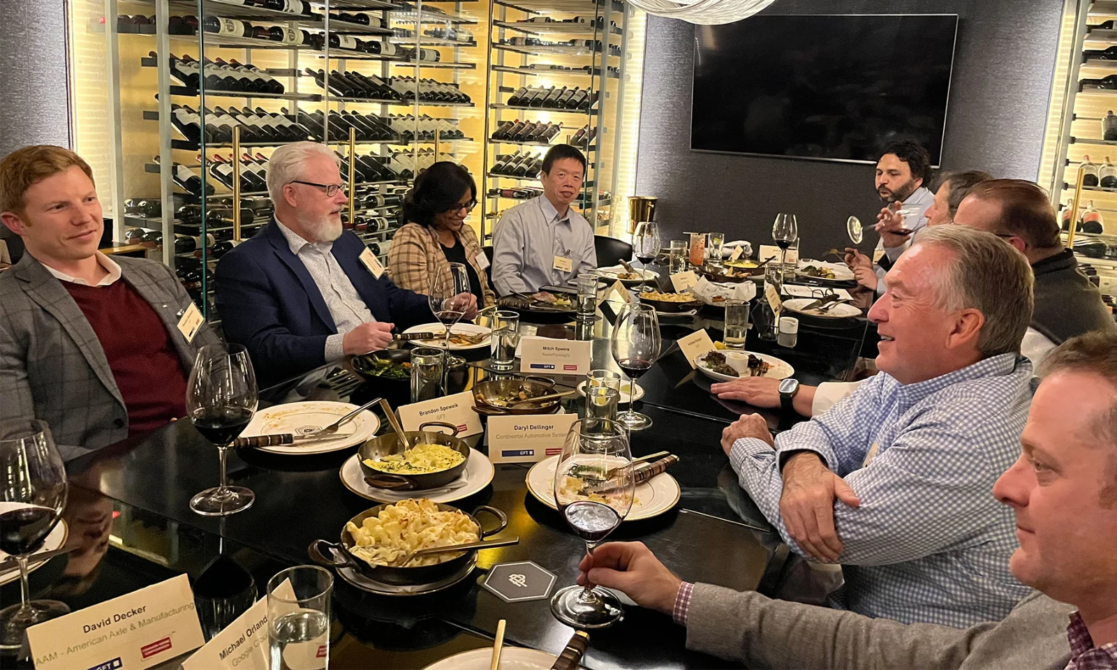 Group of business professionals enjoying an informal dinner gathering, seated around a table with wine and food in a sophisticated setting.