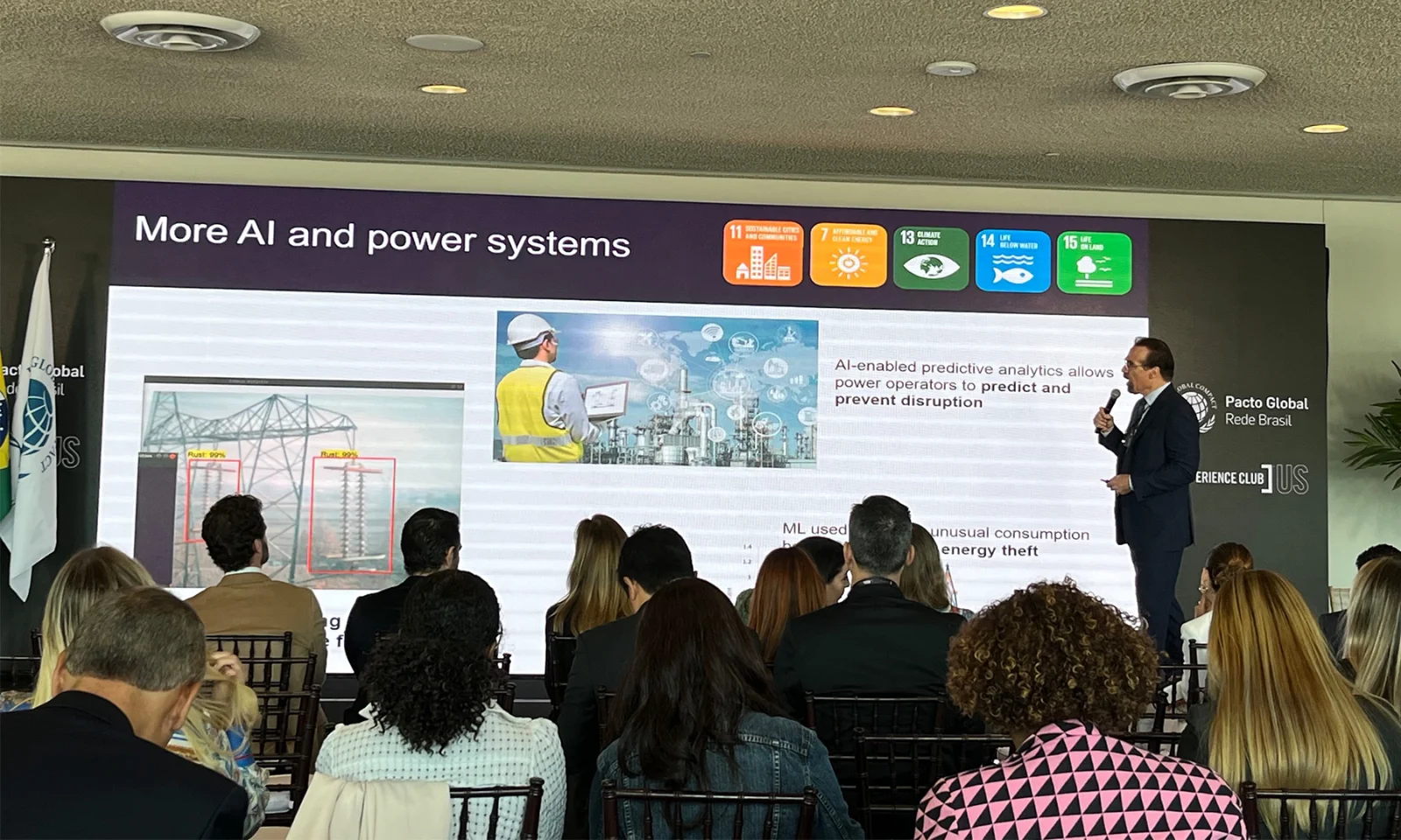 Speaker presenting on the integration of AI in power systems to an audience, with a large screen displaying information on AI-driven predictive analytics and its role in energy management.