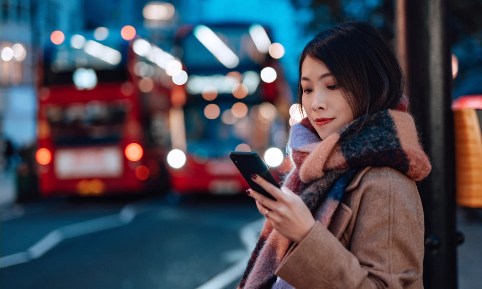 A imagem captura um viajante urbano usando um dispositivo móvel, representando a integração perfeita do banco digital e outros serviços online na vida diária. O cenário de ônibus icônicos de dois andares destaca a conectividade e a conveniência que as soluções digitais modernas, como as fornecidas pela GFT, trazem aos usuários em movimento. Apresentado no site da GFT para ilustrar o impacto da transformação digital em serviços públicos e financeiros.