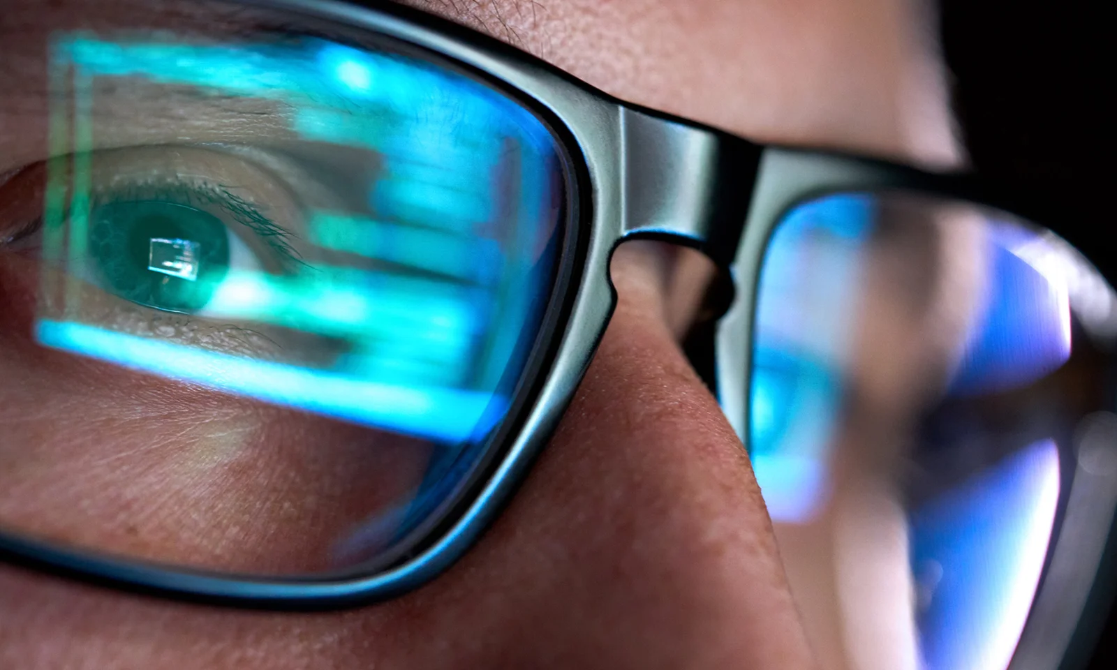 Close-up of a person wearing glasses with computer code reflecting on the lenses, emphasizing focus and concentration in coding.