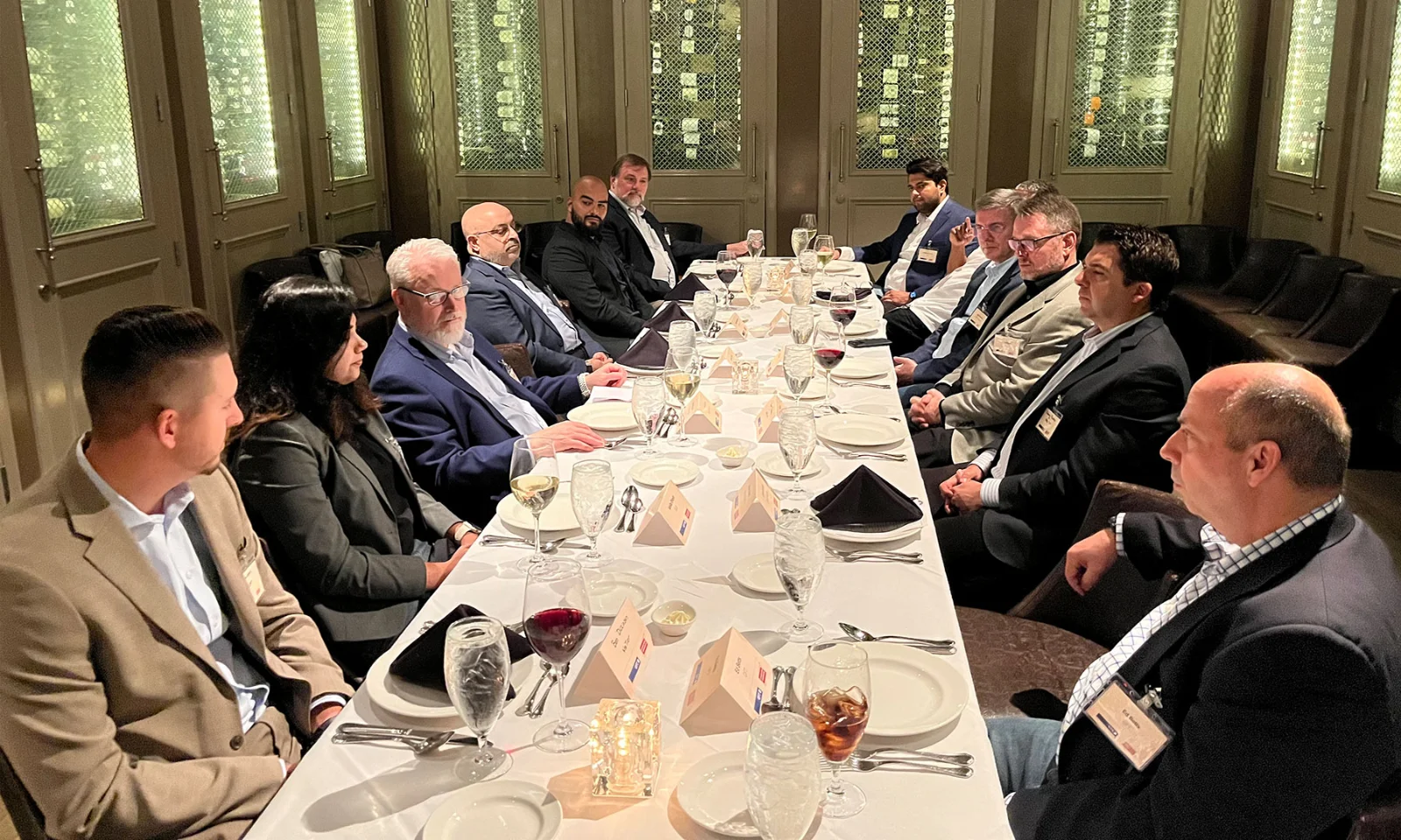 Group of business executives seated around a long table during a formal dinner meeting, discussing strategic topics in a private dining room.