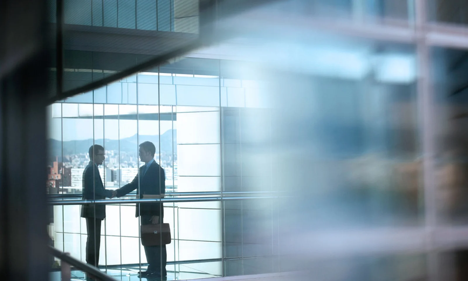 Two business professionals shaking hands in a modern office building with large glass windows, symbolising trust and successful partnership.