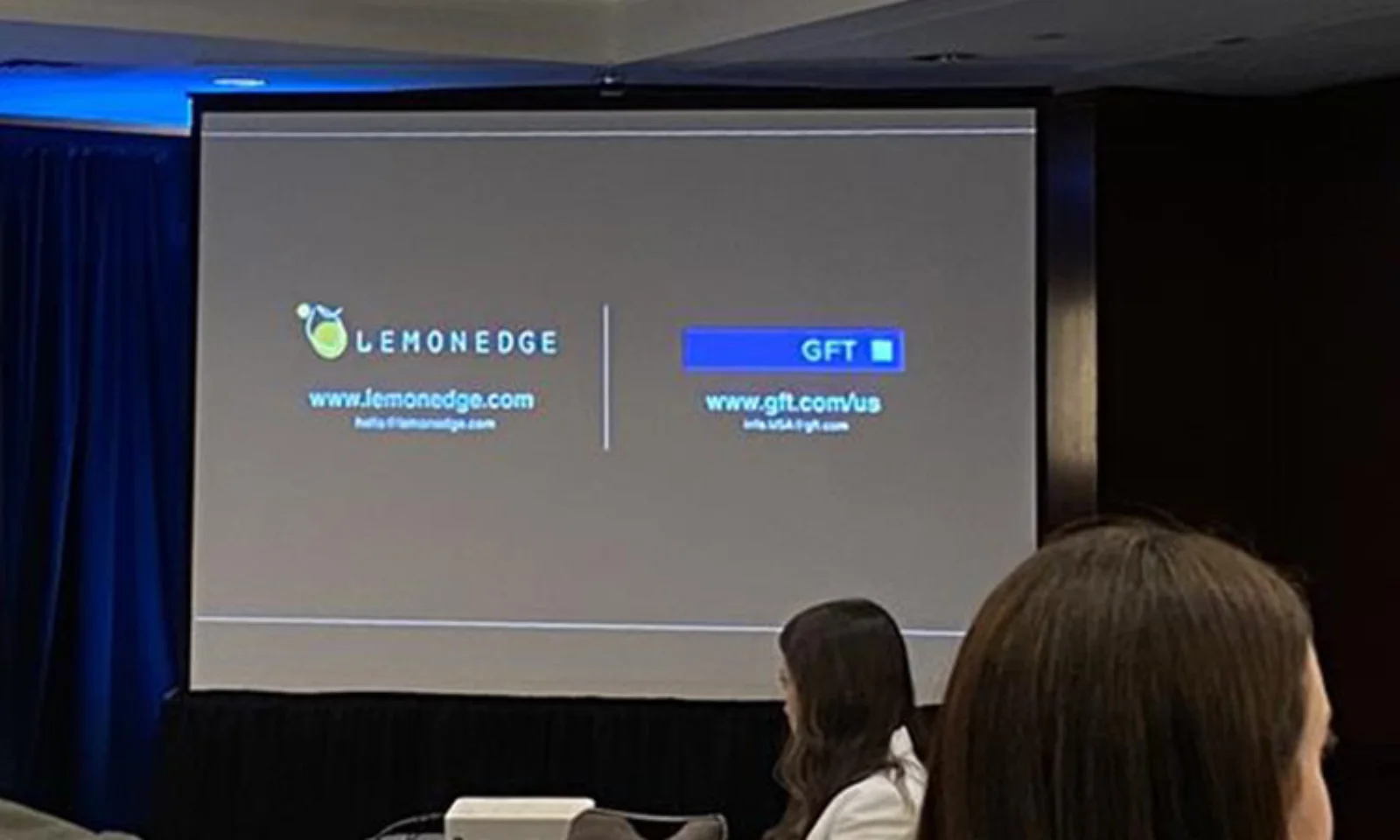 A presentation slide showing the logos of GFT and LemonEdge during an event. The slide includes their website links, www.gft.com/us for GFT and www.lemonedge.com for LemonEdge. Attendees are partially visible in the foreground, suggesting a corporate or professional setting.