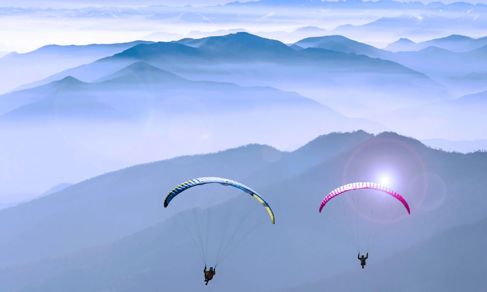 Two paragliders flying over a serene mountain landscape, symbolising freedom and exploration in a vast, open sky.