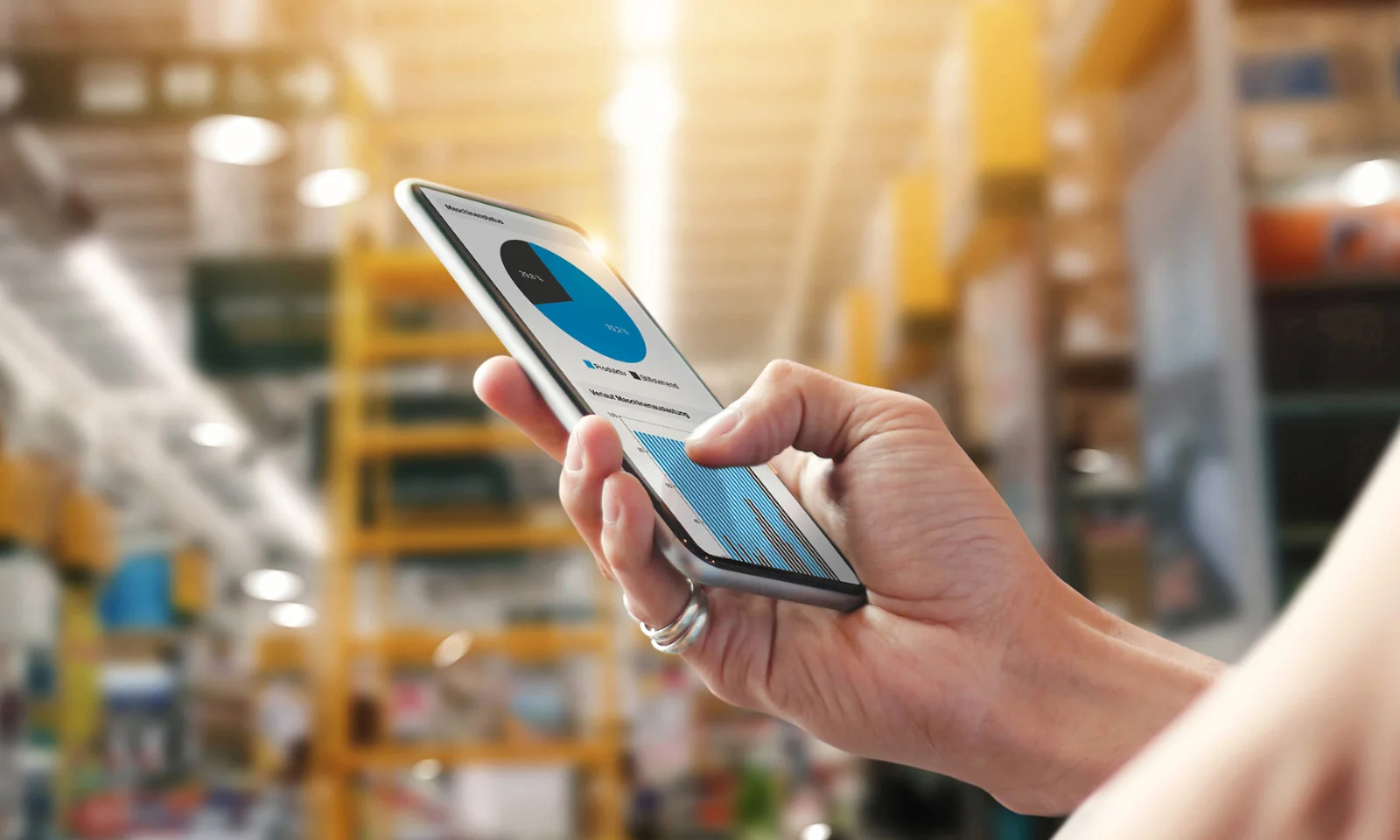 Hand holding a smartphone displaying data analytics in a modern industrial setting, representing a networked machine park.