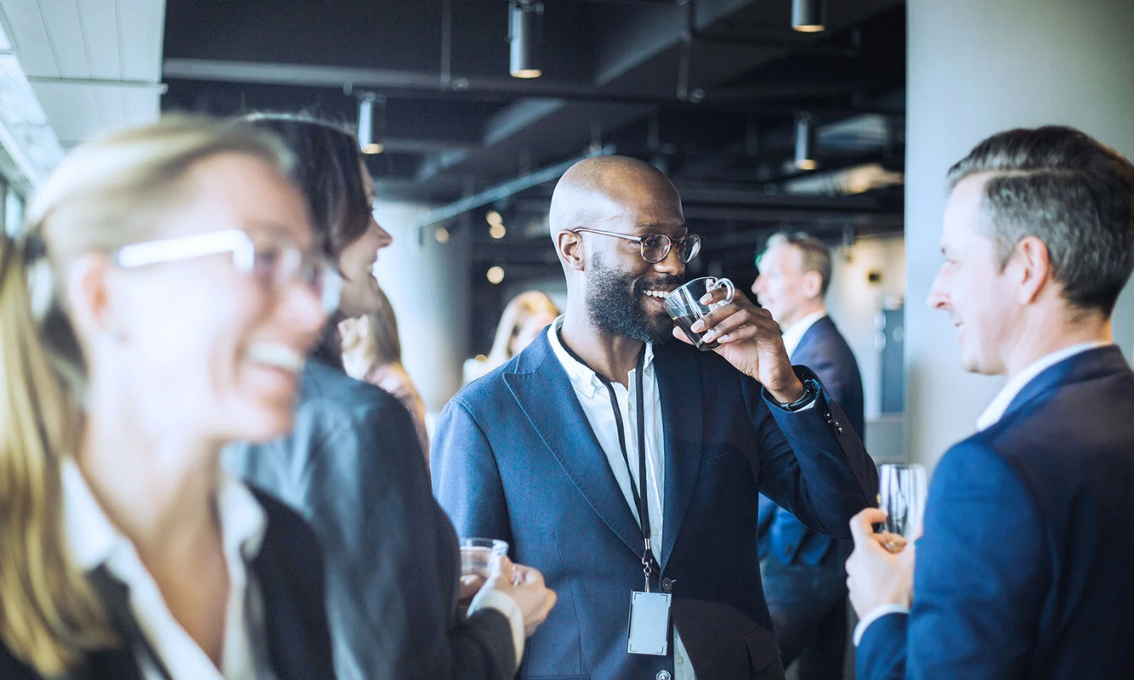 Professionals engaging in conversation and networking at a GFT event, with one man drinking coffee and others smiling and talking.